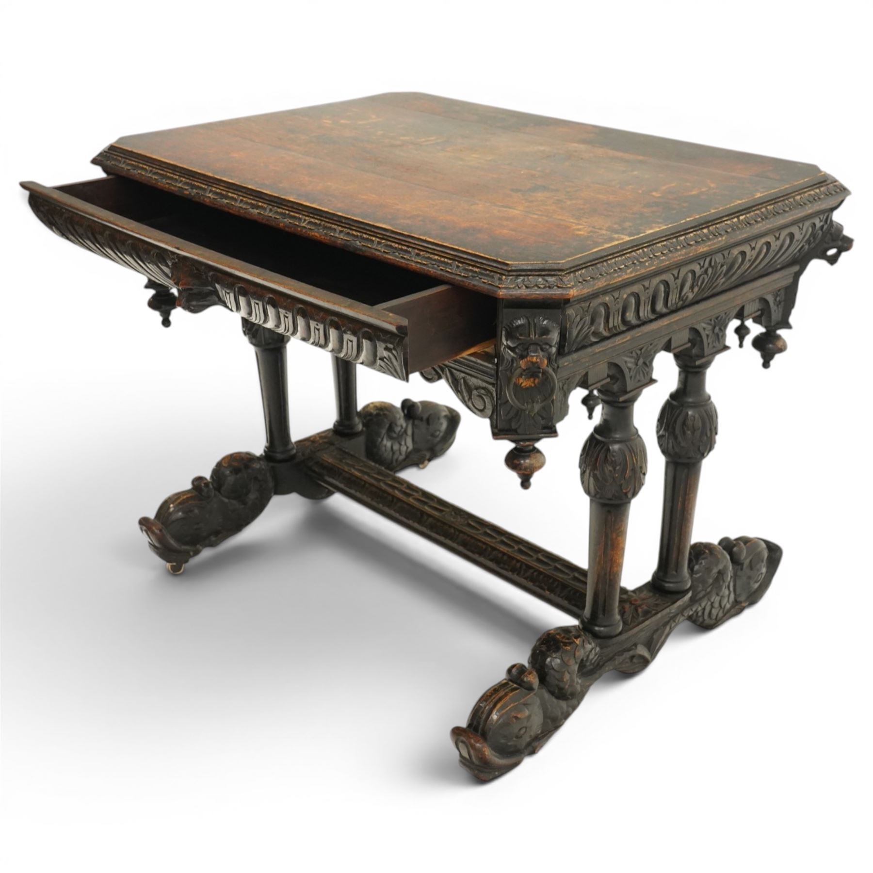 Victorian Jacobean Revival heavily carved oak centre table , rectangular top with canted corners and carved edge, fitted with single frieze drawer with central carved green-man handle with flanking gadrooning, the corners with lion masks, raised on fluted supports terminating to splayed stylised dolphin feet with castors, united by stretcher