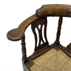 18th century country elm and oak corner chair, the shaped cresting rail terminating to swept arm resets, supported by turned columns and pierced shaped splats, over a drop-in rush seat, raised on square supports united by box stretcher