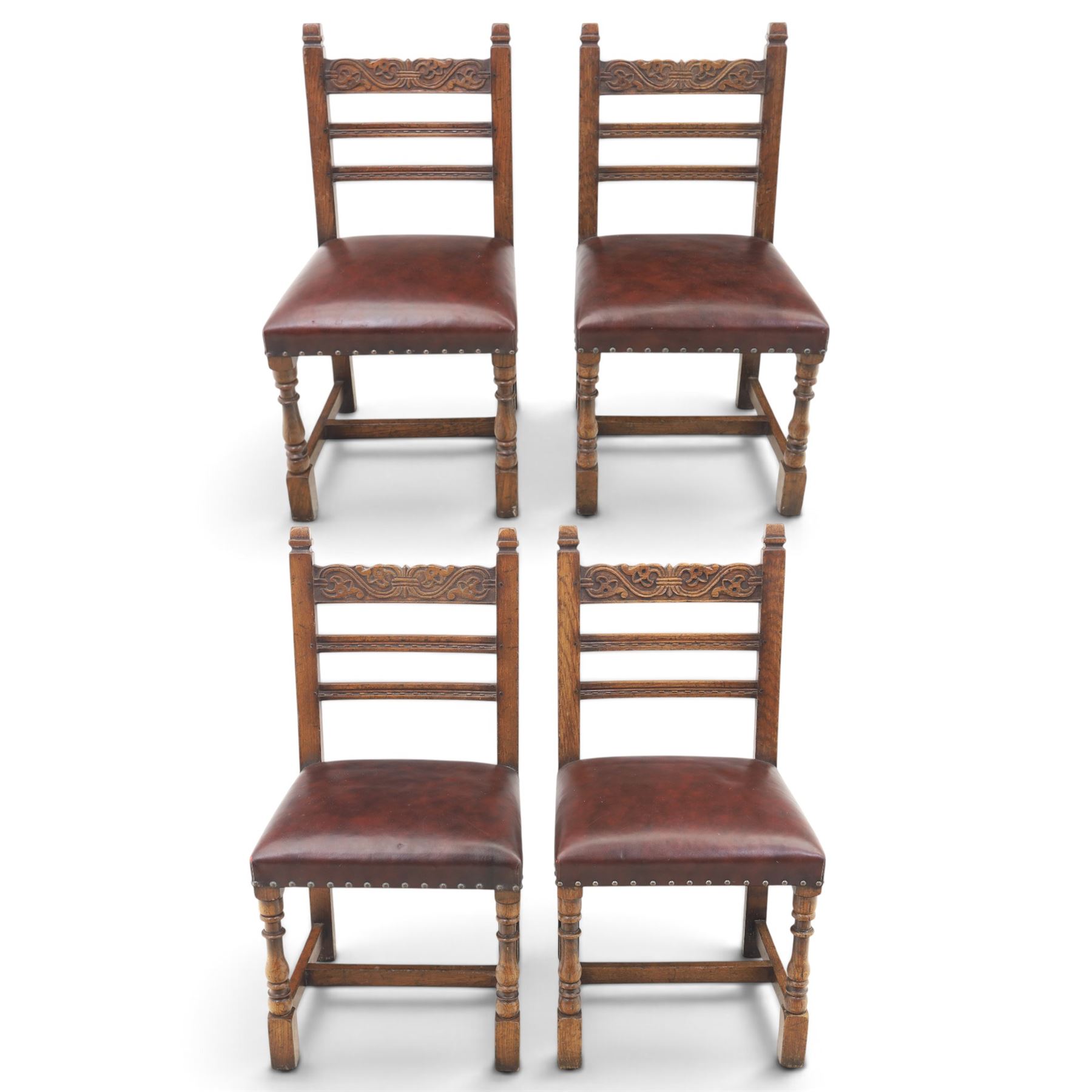 Craftsman made set of four solid oak dining chairs with leather seats, with carved cresting rail, on red leather seats with studded trim, raised on block and turn supports united by H-stretcher