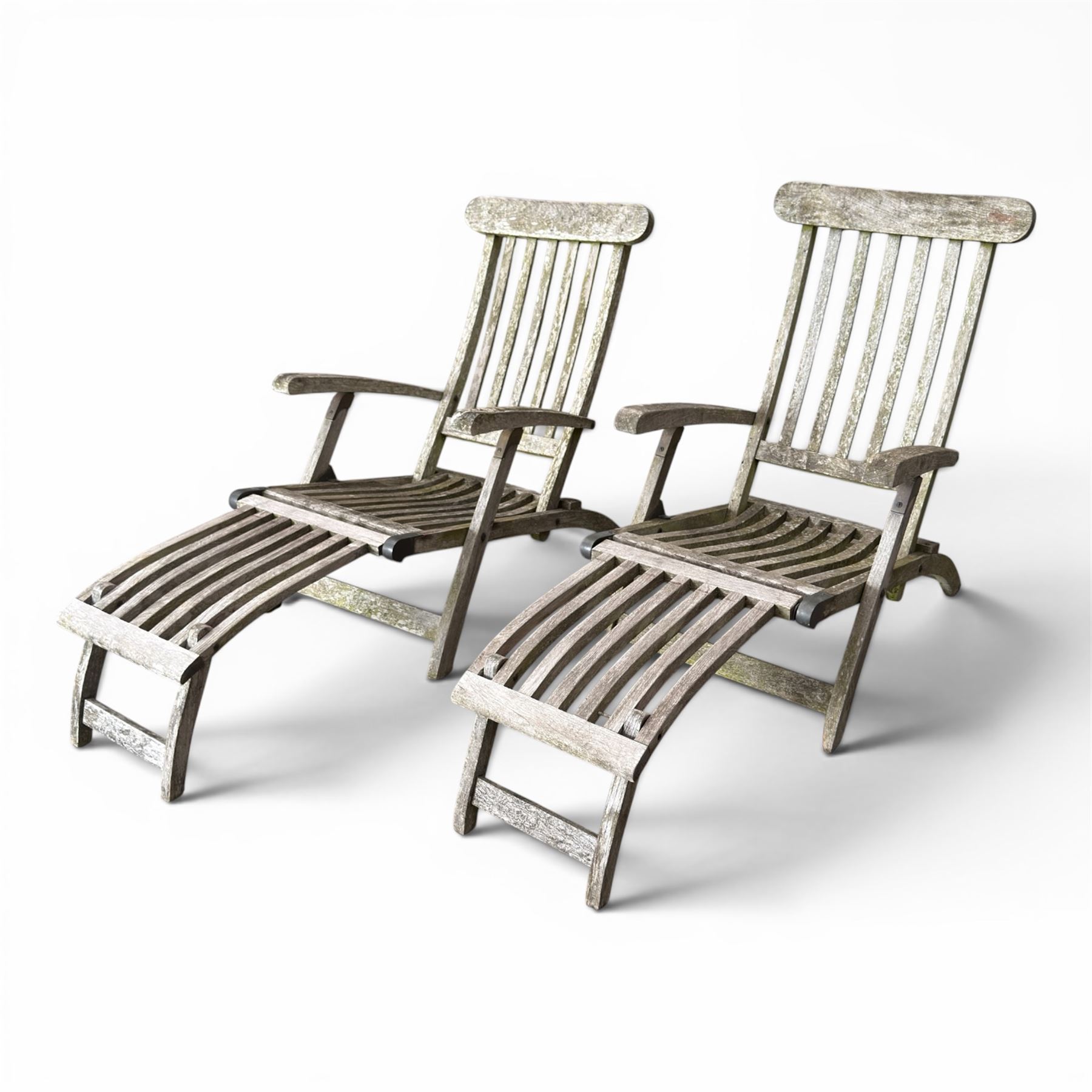 Pair of teak reclining garden steamer armchairs, each with an adjustable slatted back, curved slatted seat and footstool
