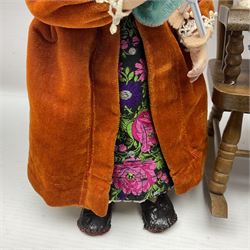 Anna Meszaros Hungary - three hand made needlework figurines - 'The Cobbler' as a child seated in a wooden rocking chair working on a removed boot H24cm; young girl standing crying holding a doll with broken head H32cm; and young girl in long dress and bonnet standing holding a doll H27cm (3)  Auctioneer's Note: Anna Meszaros came to England from her native Hungary in 1959 to marry an English businessman she met while demonstrating her art at the 1958 Brussels Exhibition. Shortly before she left for England she was awarded the title of Folk Artist Master by the Hungarian Government. Anna was a gifted painter of mainly portraits and sculptress before starting to make her figurines which are completely hand made and unique, each with a character and expression of its own. The hands, feet and face are sculptured by layering the material and pulling the features into place with needle and thread. She died in Hull in 1998.