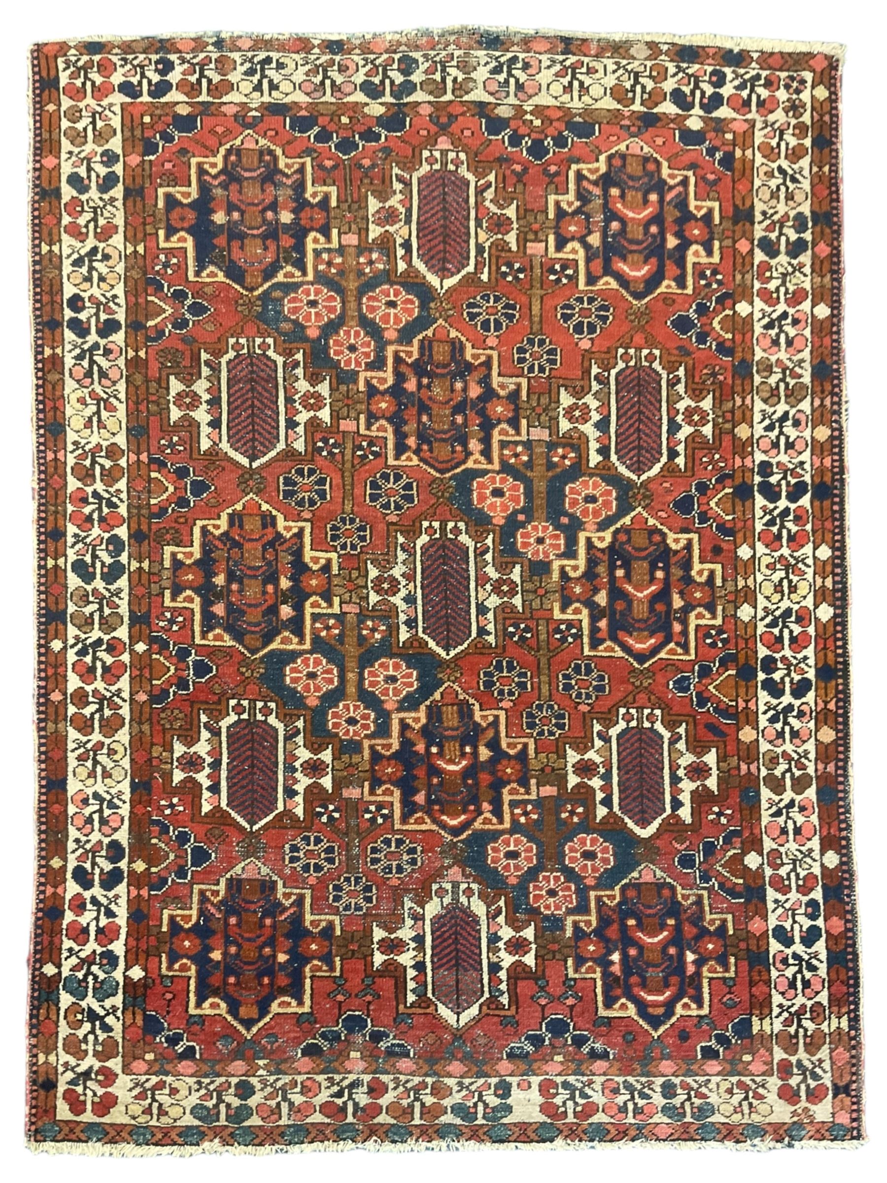 Persian crimson ground rug, the field decorated with three rows of stylised plant medallions and small flowerhead motifs, repeating floral design border with guards 