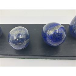 Collection of five Lapis lazuli specimen eggs, upon an ebonised wooden base, largest egg H7cm