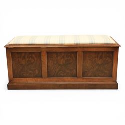 Traditional design figured elm blanket chest, with padded striped upholstered seat, over a hinged top with panelled sections below raised on a plinth base