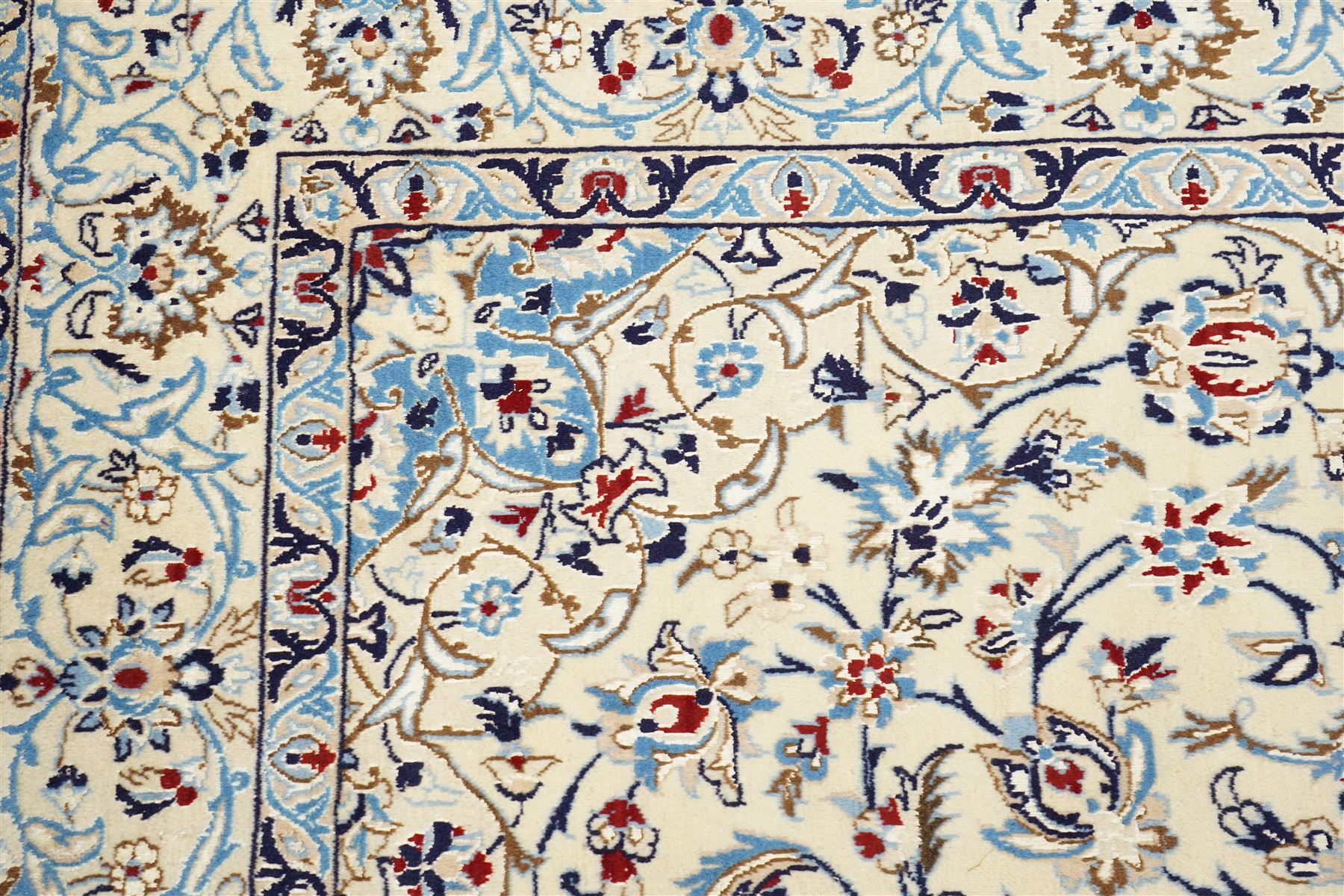 Central Persian Nain hand-knotted rug, ivory field with central medallion in tones of indigo and blue, issuing vinery, palmettes and floral sprays with conforming spandrels, dark blue main border of floral vinery and stylized palmettes, framed by multiple guard borders, with cotton fringe ends 