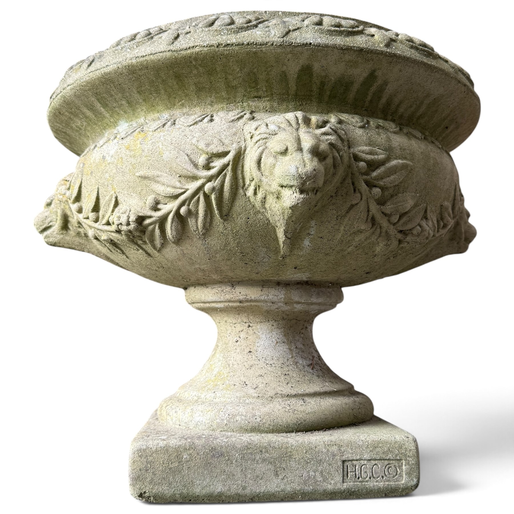Regency design weathered cast stone garden urn of kylix form, the anthemion and arrowhead moulded everted rim over a fruiting laurel and lion-mask relief decorated body, waisted socle on square base, stamped HGC