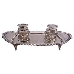 20th century silver desk stand, of shaped oblong form with oblique gadrooned rim, and twin removable glass inkwells with hinged silver covers sat within two pierced circular sections, upon four tapering feet, hallmarked William Hutton & Sons Ltd, Sheffield, date to one inkwell 1923, to other inkwell and stand date letters worn and indistinct, possibly 1911, or 1936, approximate weighable silver 7.58 ozt (236 grams)