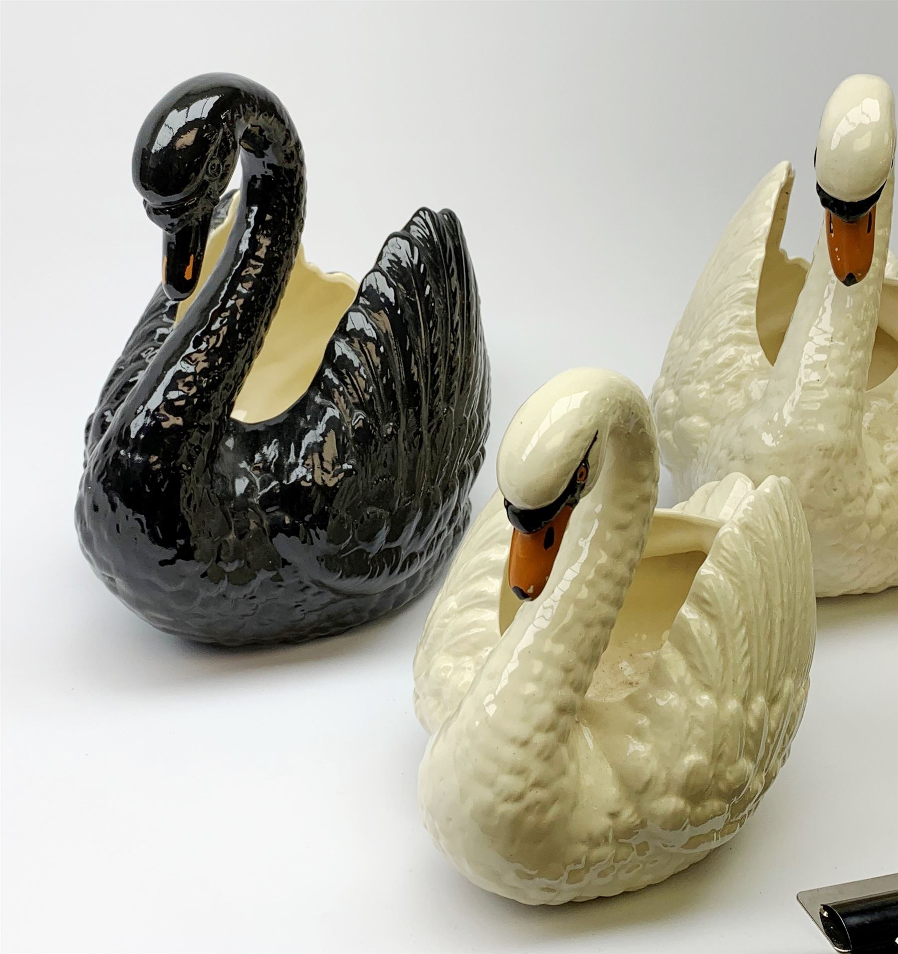 Four Dartmouth pottery jardinières or planters, modelled in the form of swans, comprising three white examples, and one black, marked beneath Dartmouth Devon England, larger examples H29cm, smaller examples H21.5cm. 
