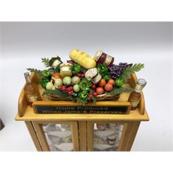 Collection of miniature dolls house grocery shop furniture and produce, comprising glazed corner counter with brass style cash register, shelved preserves unit, pies, cheese board and trays of meats, pair of white cheese counters, biscuit display with six tins, glazed preserves cabinet, pair of shop chairs and four further cheese boards complete with grapes and label flags