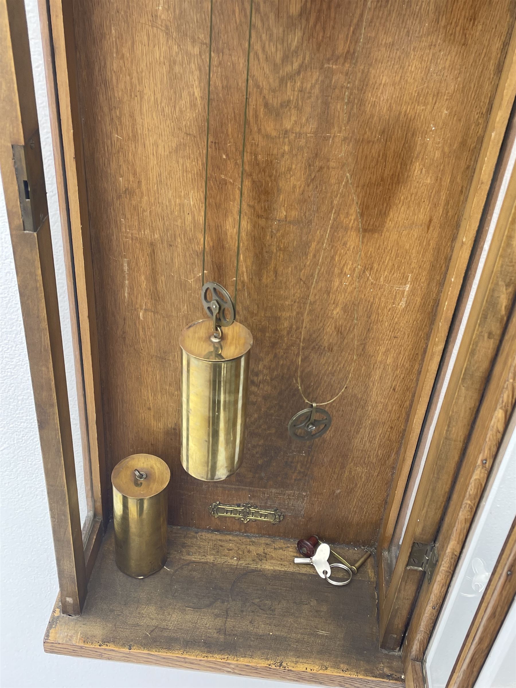 Early 20th century oak cased wall clock, the door glazed with circular convex dial glass and bevelled upright panes, circular brass and silvered Roman dial, twin train driven movement striking on coil 