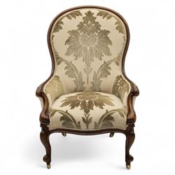 Victorian mahogany framed spoon back armchair, the shaped and padded back over serpentine seat upholstered in a floral damask pattern fabric within a moulded frame carved with scrolled arms, raised upon cabriole front legs with scroll feet on porcelain castors 