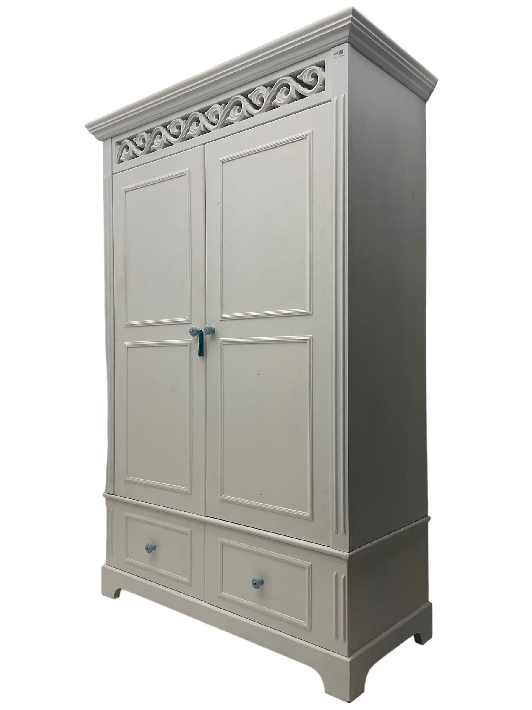 White painted double wardrobe, pierced scrolling foliate frieze over two doors enclosing hanging rail and two shelves, two drawers fitted to base, with blue ceramic handles