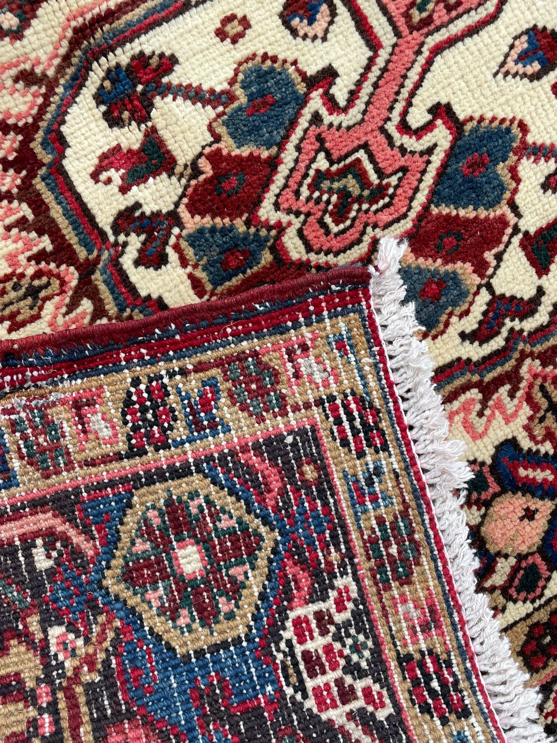 Persian Heriz red ground rug, central scrolled medallion on dark ground decorated with floral motifs, the surrounding field decorated with stylised plant motifs and smaller geometric symbols, guarded border with repeating pattern punctuated with rosettes and flower heads 