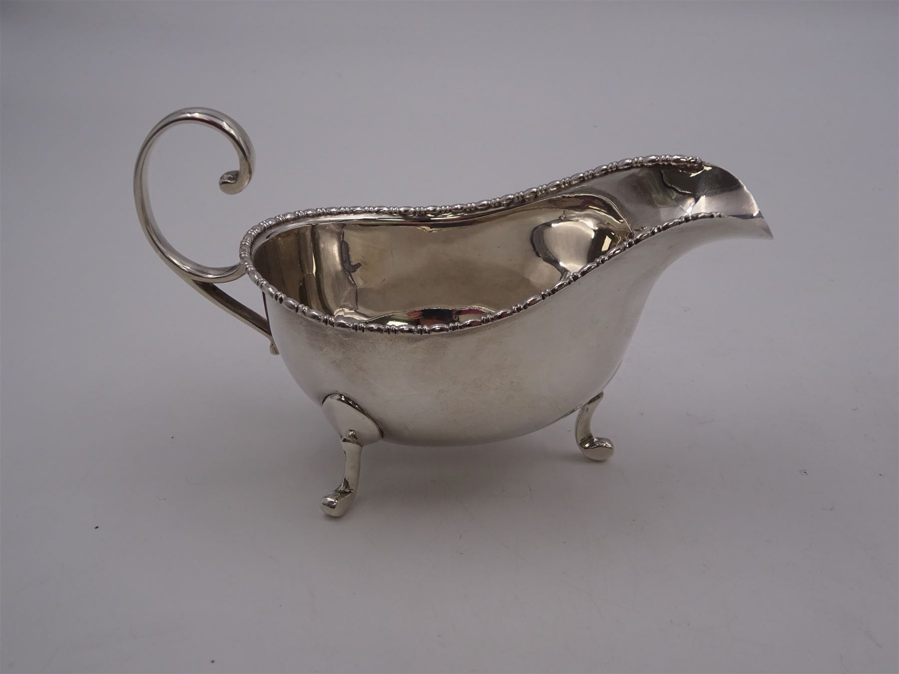 Pair of 1930s silver sauce boats, of typical plain form, each with bead and dart rim and flying scroll handles, upon three pad feet, hallmarked Walker & Hall, Birmingham 1935