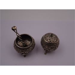 Indian silver pepper shaker, of spherical form, with embossed floral and foliate decoration, upon three pad feet, together with a similar Indian silver open salt and an Indian silver salt spoon with twisted serpent handle and shell bowl