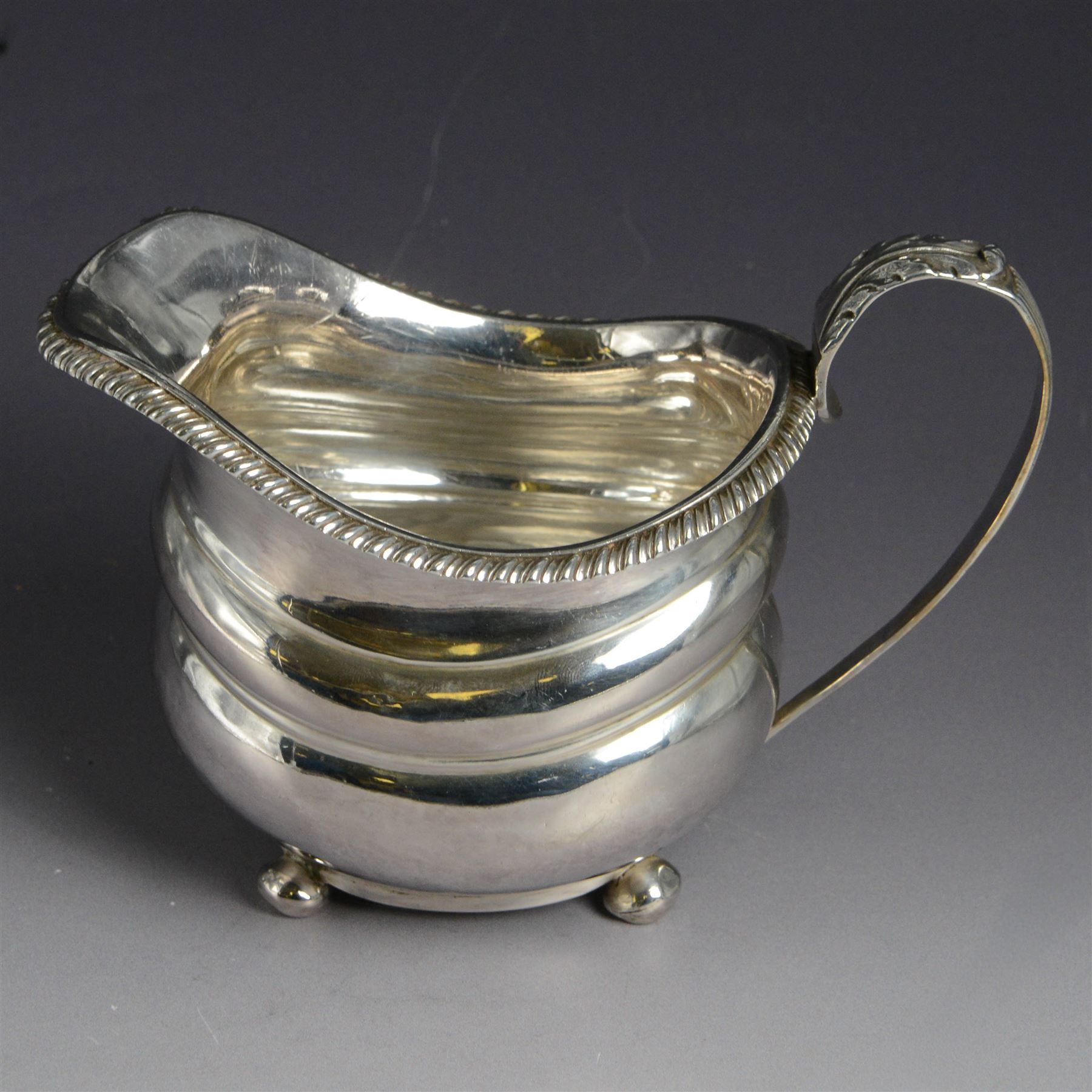 George III silver milk jug, of oval form with oblique gadrooned rim and acanthus leaf capped handle, upon four bun feet, hallmarked London 1819, maker's mark worn and indistinct, H10cm