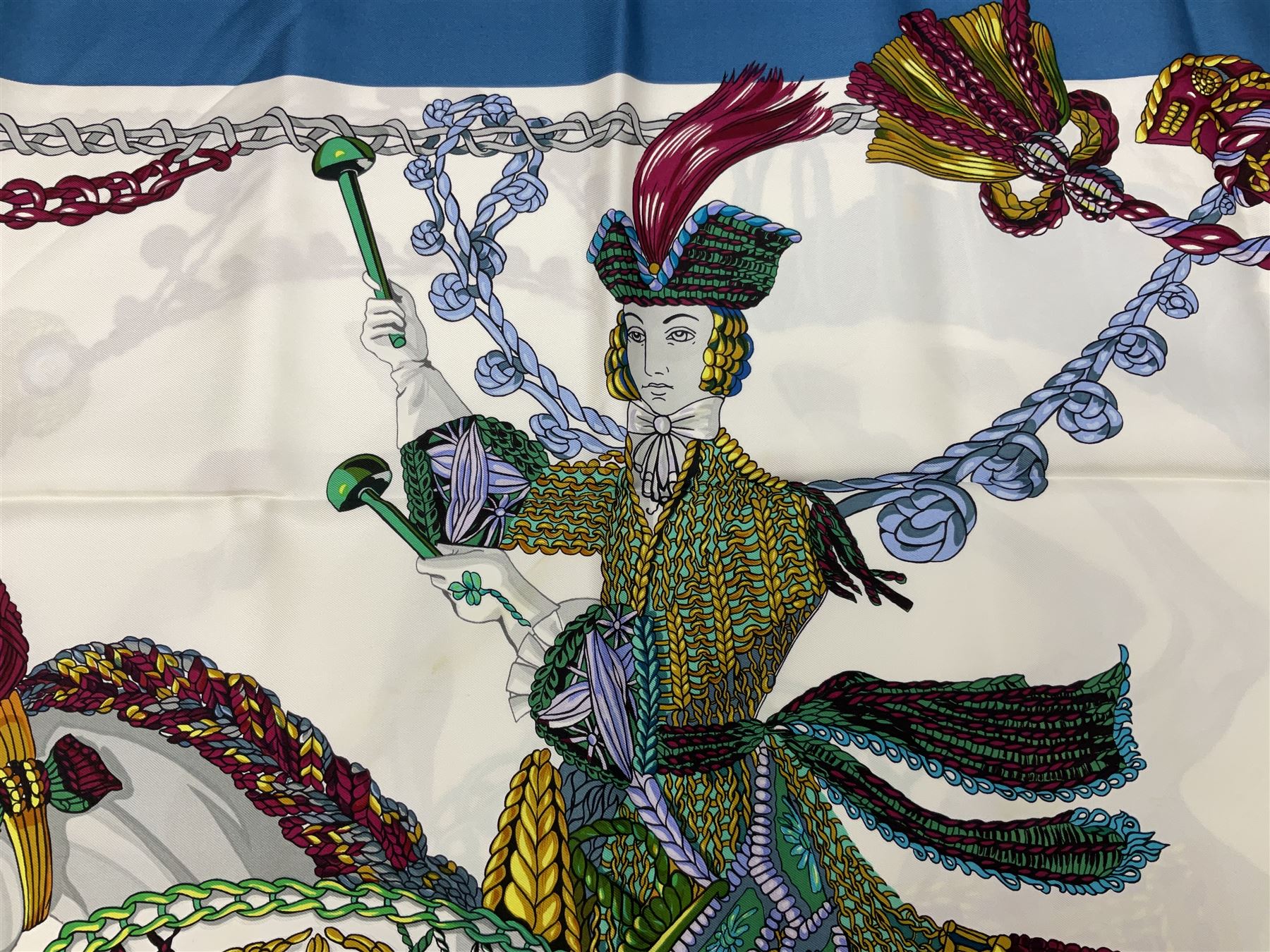 Hermès 'Le Timbalier' silk scarf, designed by Francoise Heron in 1961, printed with a central image of a gentleman on horseback donning extravagant dress, on white ground surrounded with colourful stylised knotted ropes, contained within peacock blue border, with rolled hand stitched edges and Hermes material label, 87cm square