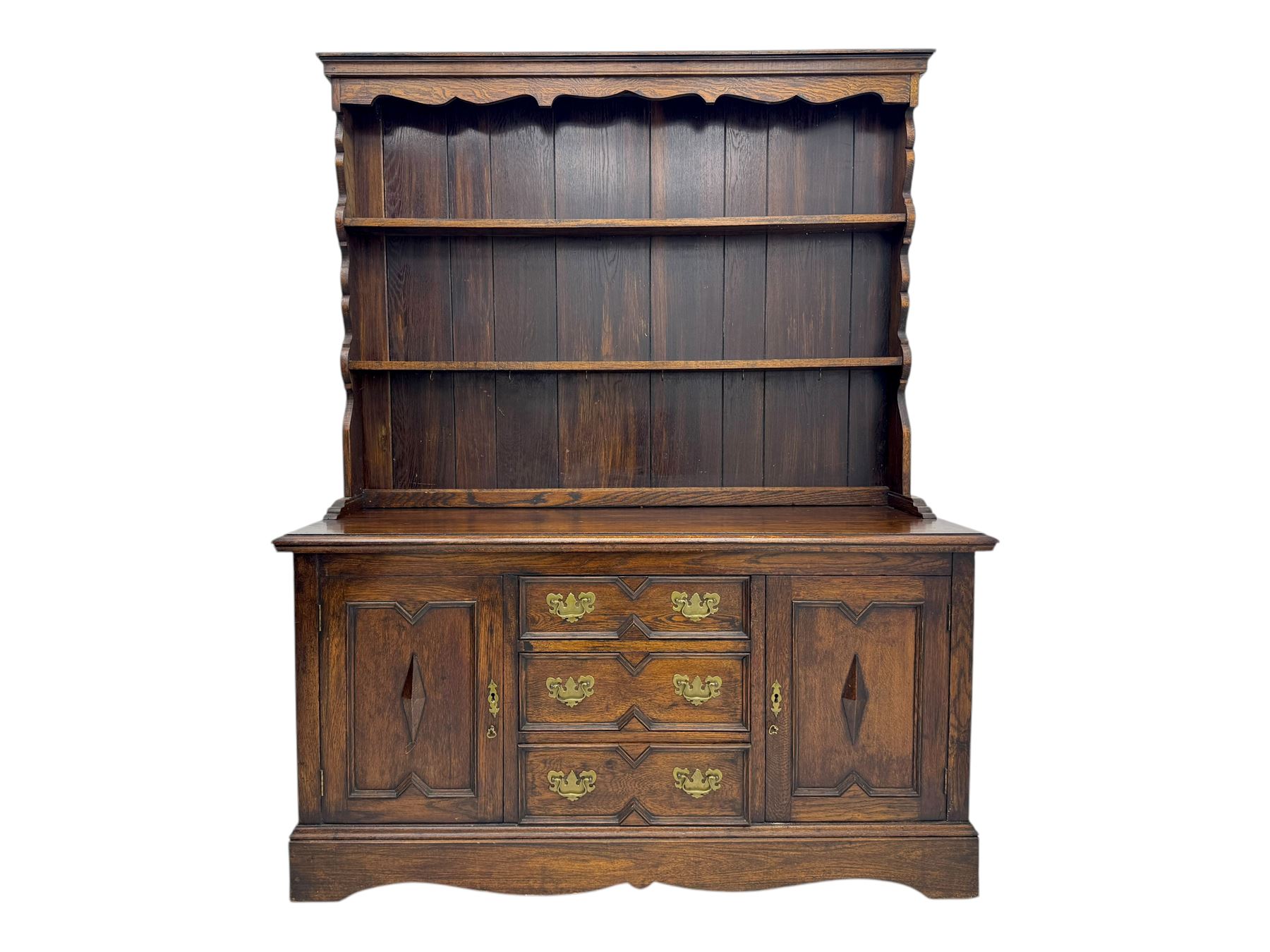Late 19th century oak dresser, the upper section with two shelves beneath a shaped cornice, the lower section with a central bank of three drawers flanked by cupboard doors, all decorated with geometric diamond motifs, the drawers fitted with brass handles, raised on a shaped plinth base