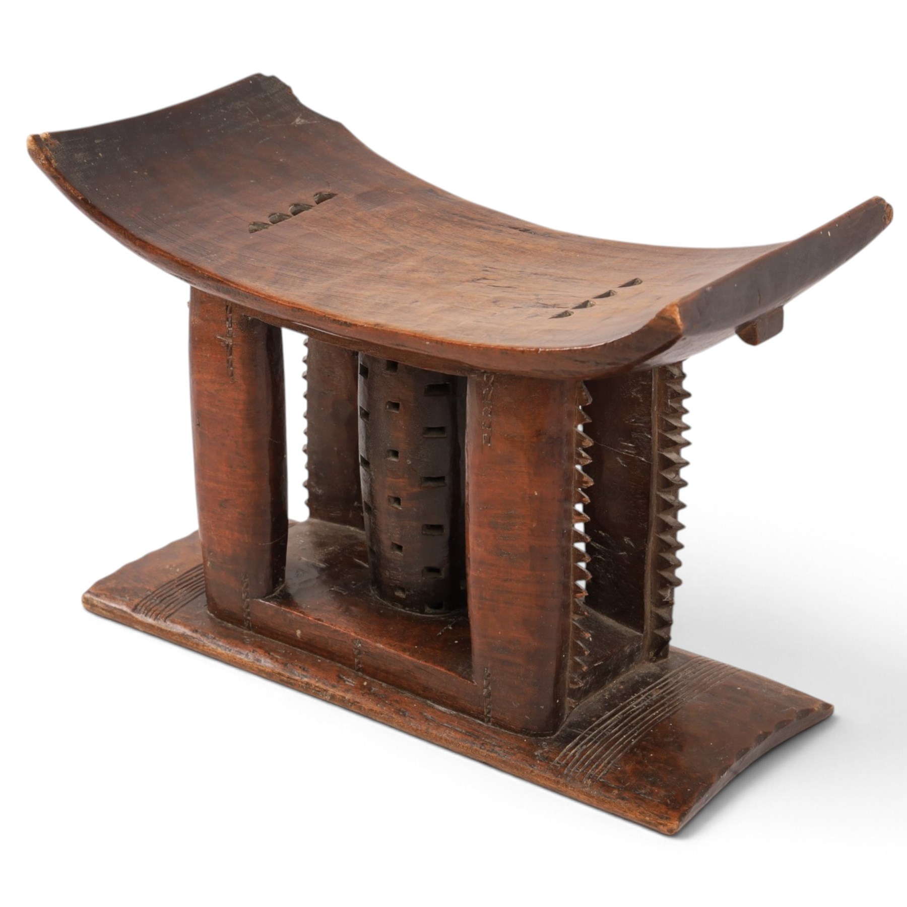 African carved hardwood headrest, having flared edges, raised on a stepped plinth base with further carved detailing, H34cm