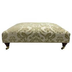 Large rectangular footstool, upholstered in cream self-embossed fabric on turned mahogany feet with brass cups and castors