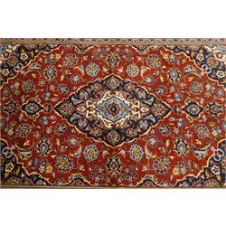 Central Persian Kashan hand-knotted rug, madder red field with central articulated cusped medallion in ivory and sky blue, issuing network of scrolling arabesques palmettes and floral sprays with conforming spandrels, indigo main border of scrolling vinery and stylized palmettes, framed by multiple guard borders, with cotton fringe ends  