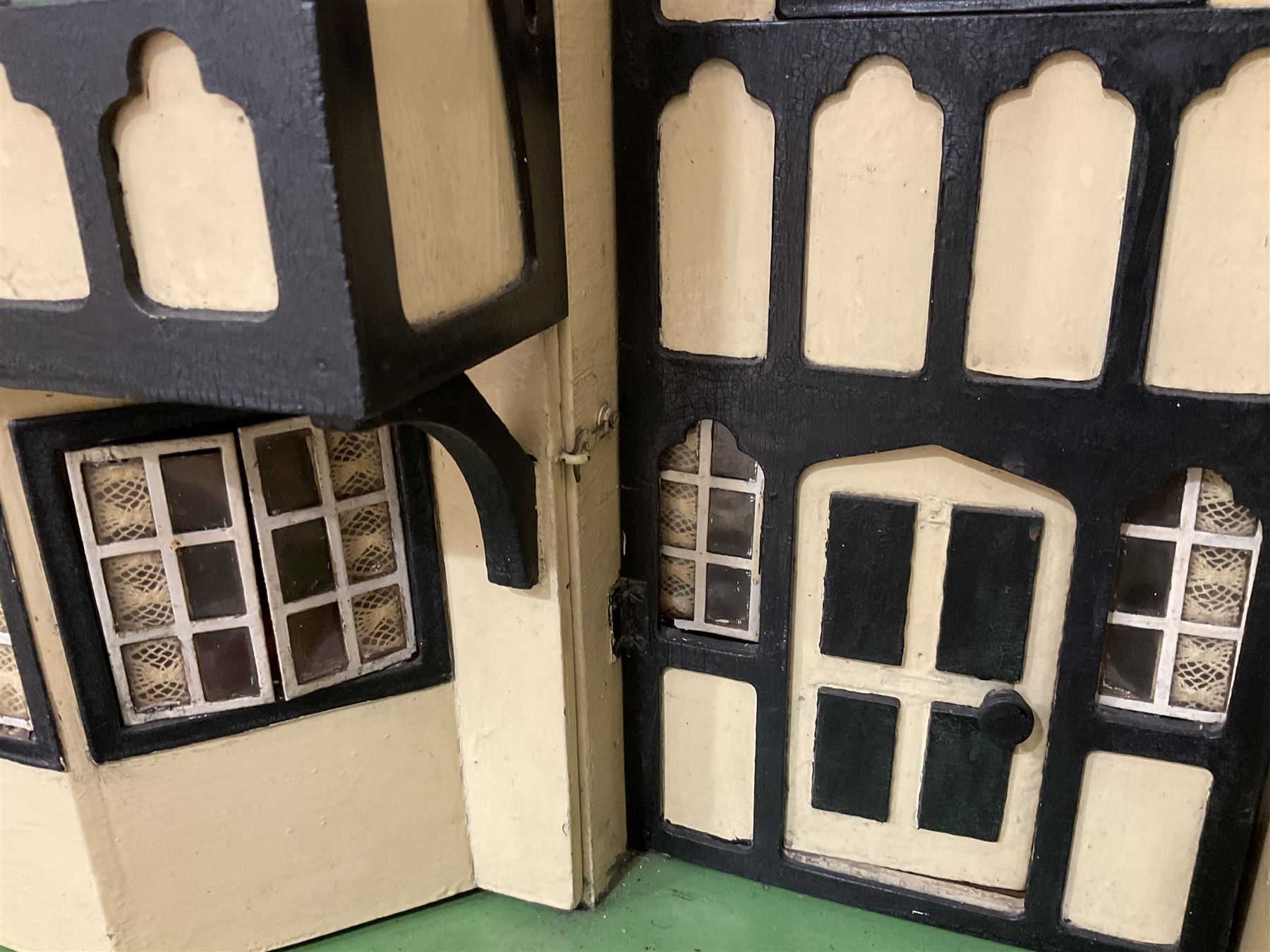 Large Tri-ang No.93 doll`s house in the 'Stockbroker's Range' c1935; two-storey double-fronted Tudor design, half timbered gables, two-storey bay windows, cream and mock shrubbery to front, opening metal framed windows with green shutters, red simulated tiled roof with chimney, integral garage with opening doors, front elevation has four hinged doors opening to reveal two bedrooms with fire places, living room, bathroom and kitchen with built in dresser and sink, entrance hall and staircase, side entrance with porch and seat and sun dial over on chimney stack; some wiring for electrical lighting; metal Tri-ang Toys disc verso; comprehensively furnished H66cm L117cm D43cm