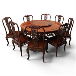 20th century Chinese ornately hardwood dining table and chairs, circular table with 'Lazy Susan' top with pierced carved frieze, raised on a quadriform base with carved foliate detail, the chairs en suite with carved pierced detailing  