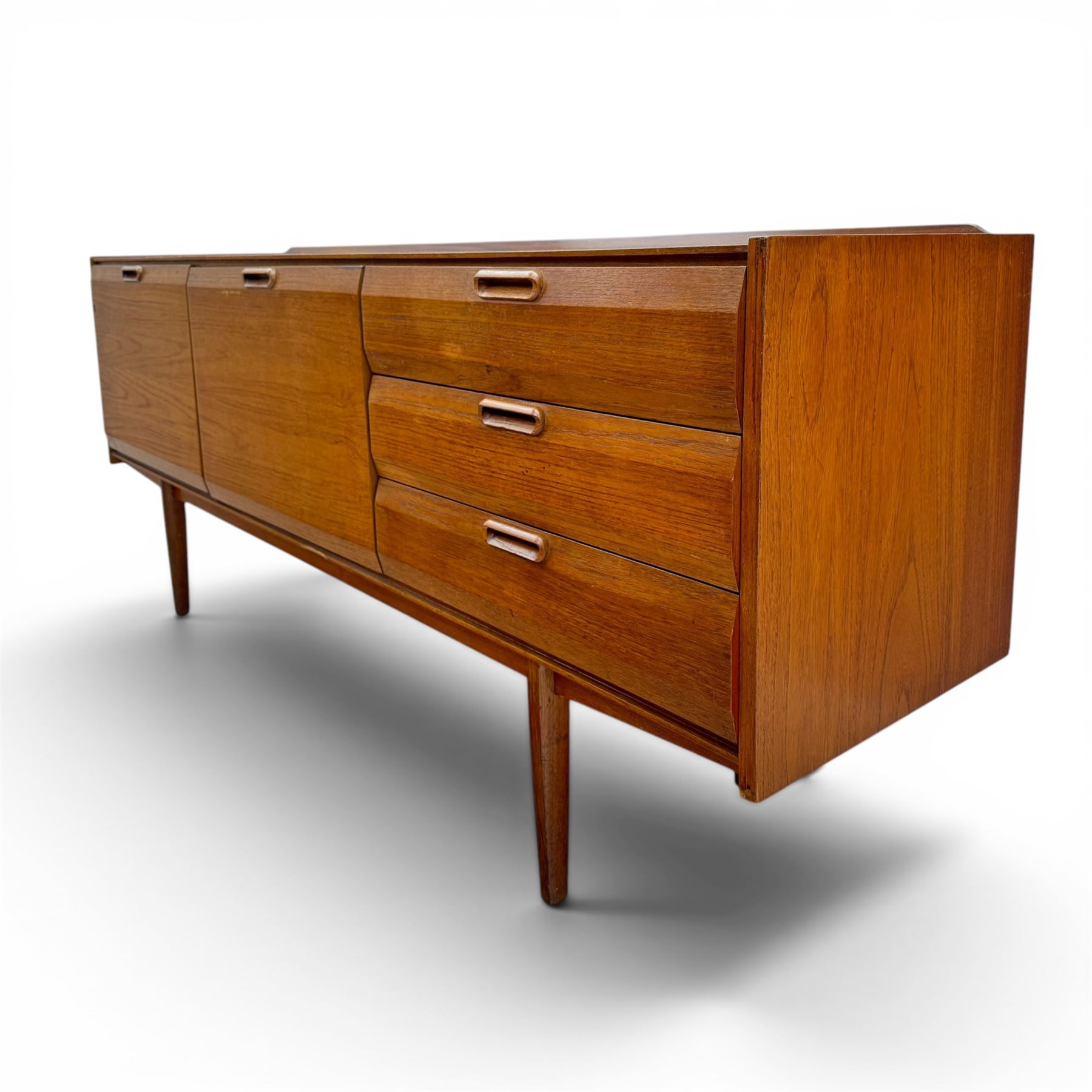 BCM (Bath Cabinet Makers) - mid-20th century teak sideboard, rectangular top with back gallery, left hand side fall front cupboard, centre cupboard opening to reveal a shelved interior, the right side with a bank of three drawers one fitted for cutlery, raised on inset tapering supports