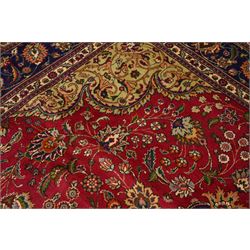 North East Persian Meshad hand-knotted carpet, crimson field with central lobed medallion in tones of indigo, ivory and soft blue, with an all-over arrangement of scrolling vinery, palmettes, and floral  sprays, conforming spandrels, main border of stylized floral vinery framed by multiple guard borders, with cotton fringe ends