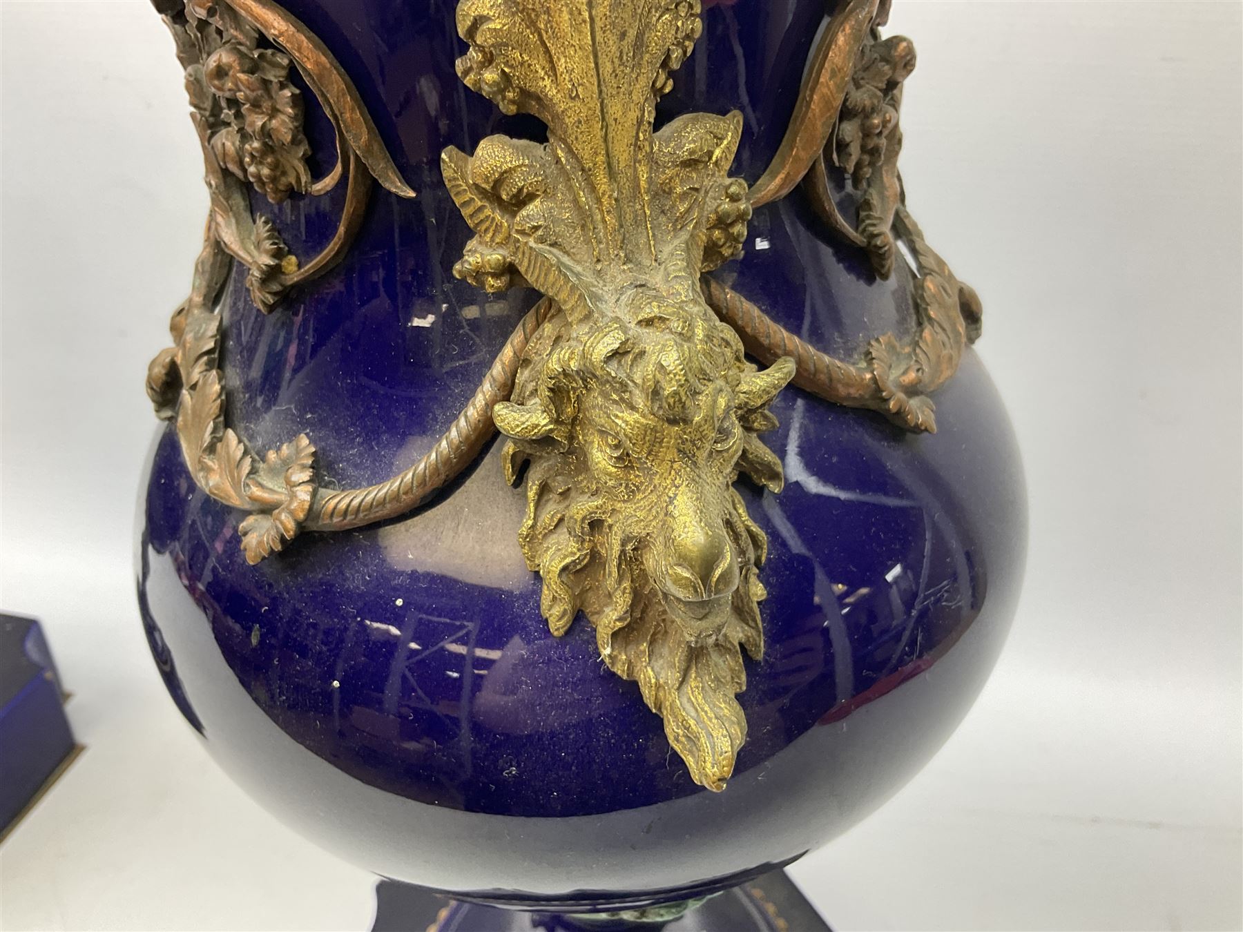 Pair of French large cobalt blue lidded urns, probably 19th century, the body decorated with ormolu ram's heads and ornate foliate design, the domed cover with brass berry finial, raised upon pedestal base with beaded decoration upon shaped plinth, H52cm