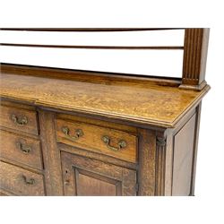 George III oak dresser, projecting dentil cornice over three heights plate rack enclosed by fluted uprights, the dresser fitted with five drawers and two panelled cupboards, canted corners with fluted quarter columns, on bracket feet