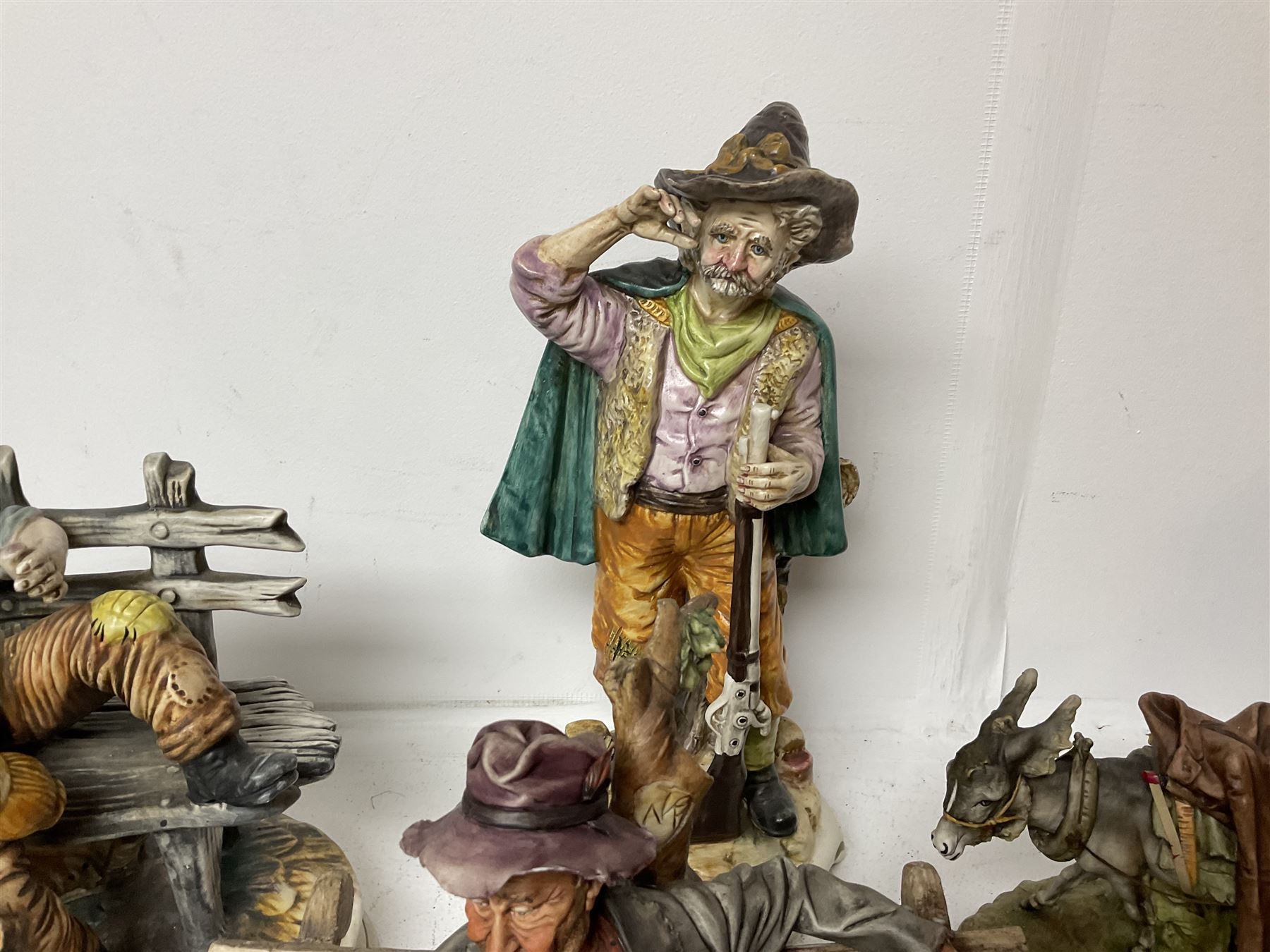 Group of Capodimonte figures, to include musical organ grinder with donkey and monkey, two tramp figures on benches, man with gun and choir boy and girl figures