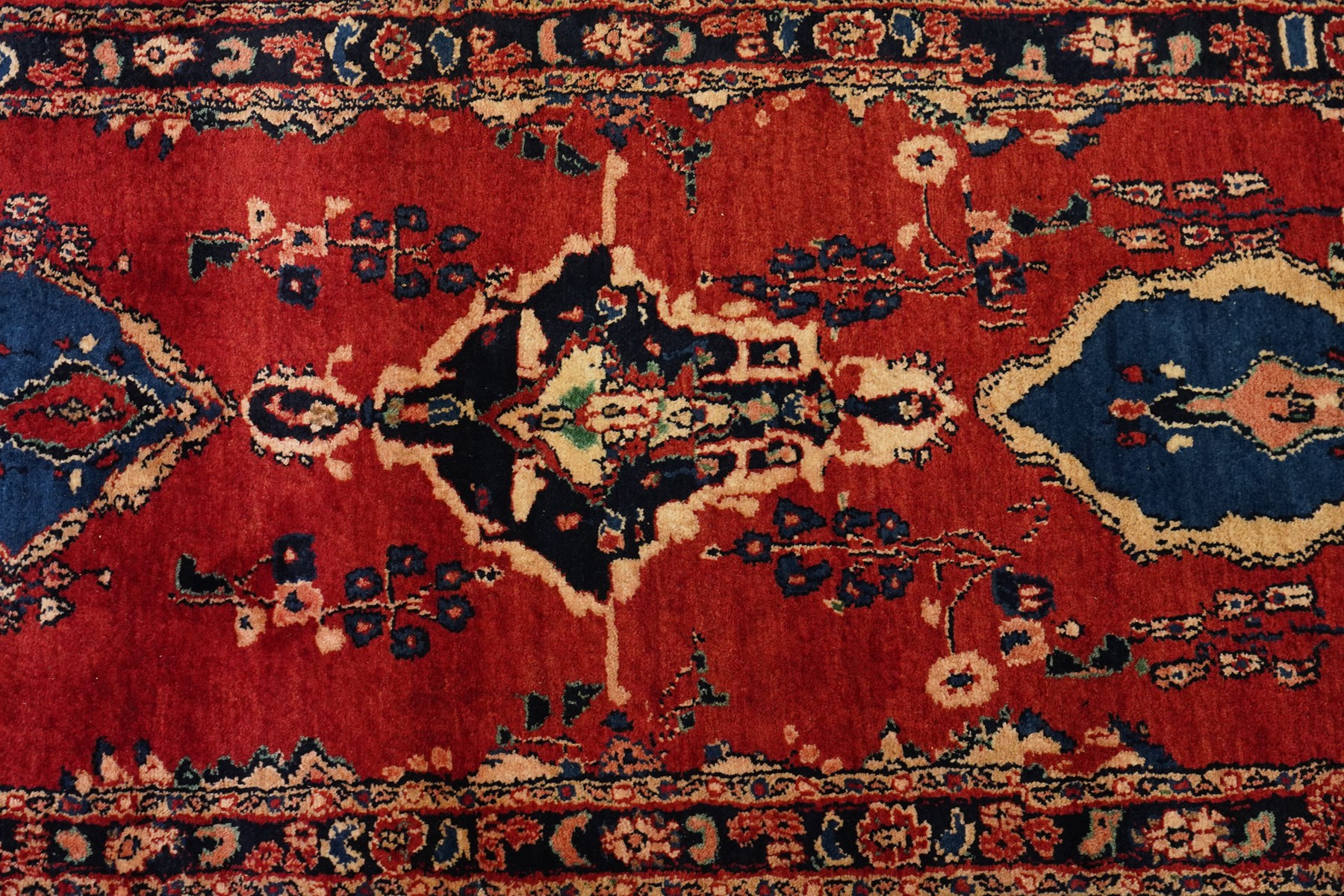 Persian Hamadan runner rug, the vermilion ground decorated with a row of ivory and indigo medallions interspersed with stylised flowering plants, indigo spandrels, enclosed by an indigo floral border and narrow patterned guard stripes