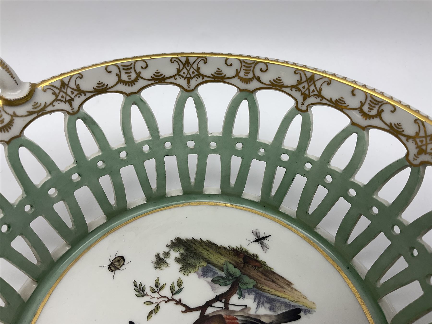 Pair of 19th century German openwork chestnut baskets, with twin handles and scrolling gilt border and star rim, painted to the centre with birds and insects, D22cm 