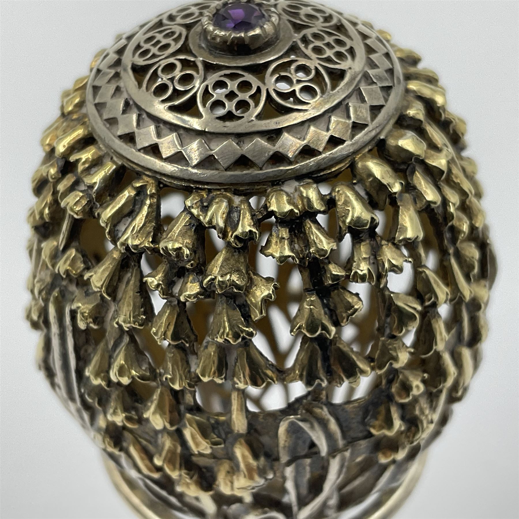Modern silver limited edition Easter egg, no. 70/500, the gilt openwork body decorated with cascading bluebells and hinged cover with pierced circular panel set with a single faceted purple stone, opening to reveal a gilt interior, upon silver stand with three scrolling pad feet, each hallmarked St James House Company, London 1981, height including stand 8cm