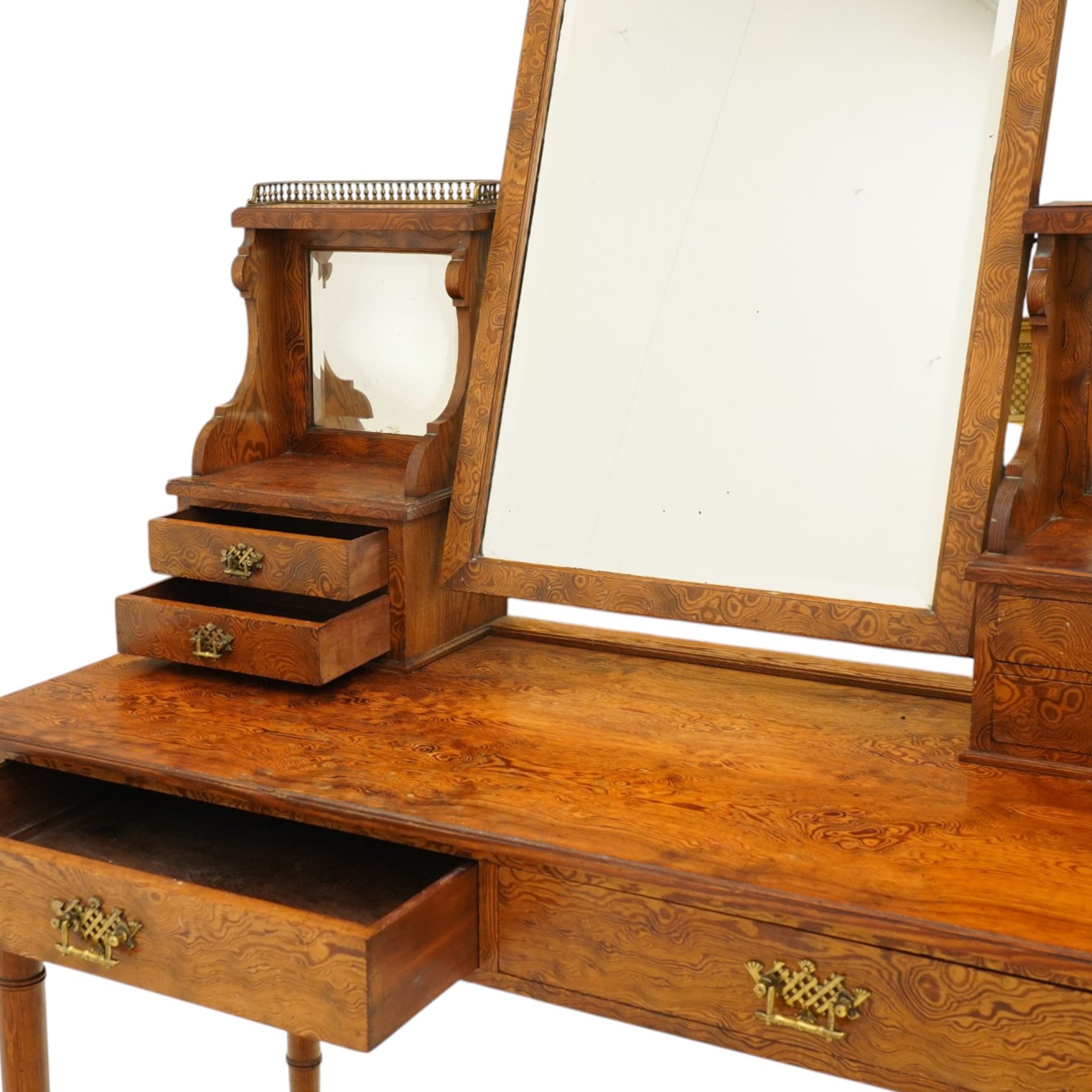 Late Victorian figured pitch pine dressing table, the rectangular swing mirror with shaped cresting flanked by mirrored superstructures, one with a three-quarter galleried shelf, fitted with two drawers, rectangular over two frieze drawers fitted with pierced brass lattice handle plates, raised on ring-turned tapering legs with brass castors