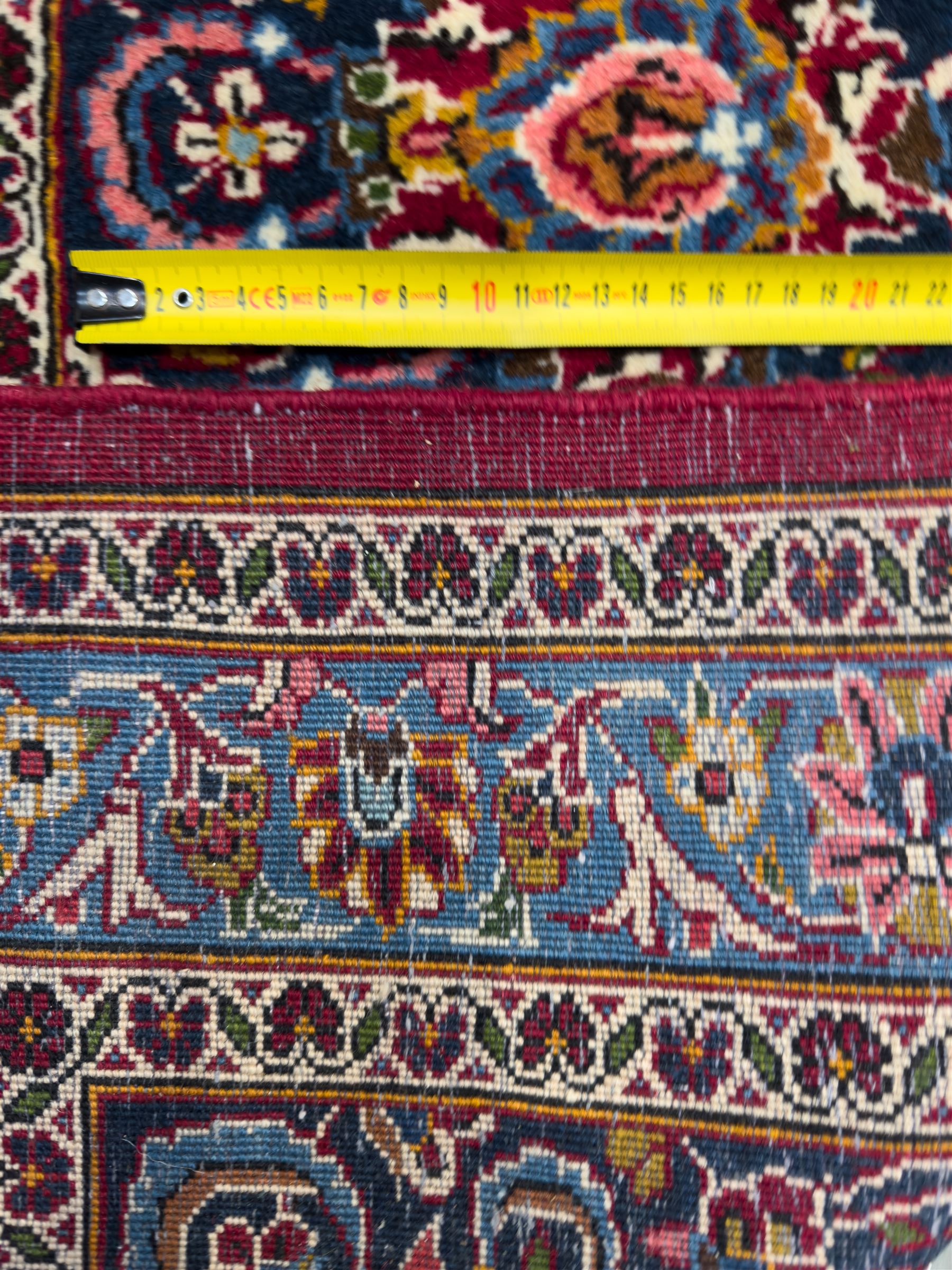 Central Persian Kashan hand-knotted carpet, madder red field with an intricate design of scrolling vines, palmettes, and rosettes with a central lobbed medallion with pendant motifs in shades of blue and ivory, and spandrels all within a blue-ground border of palmettes and flowerheads between multiple guard borders, 450cm x 335cm 