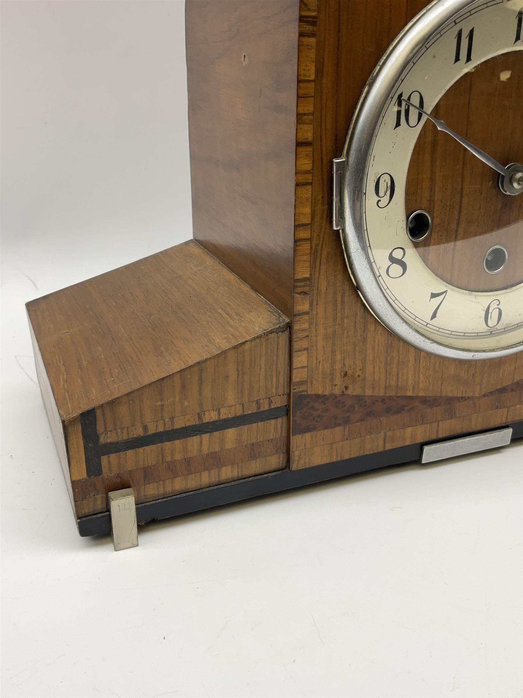 A 1930’s eight-day three train art deco Westminster chiming mantle clock with a Haller & Benzing (German) movement chiming the quarters on five underslung gong rods, silver effect chapter ring with upright Arabic numerals and minute track, strike/silent lever, chrome spun bezel with a convex glass, pierced chrome hands, walnut veneered case inlaid with cross banding and inlaid with amboyna and ebony.
With pendulum.
Haller & Benzing were a short-lived firm of German clockmakers with a factory in Villingen-Schwenningen from 1918 to 1929, mainly known for producing industrial clocks, their domestic clocks are not as well known. 
