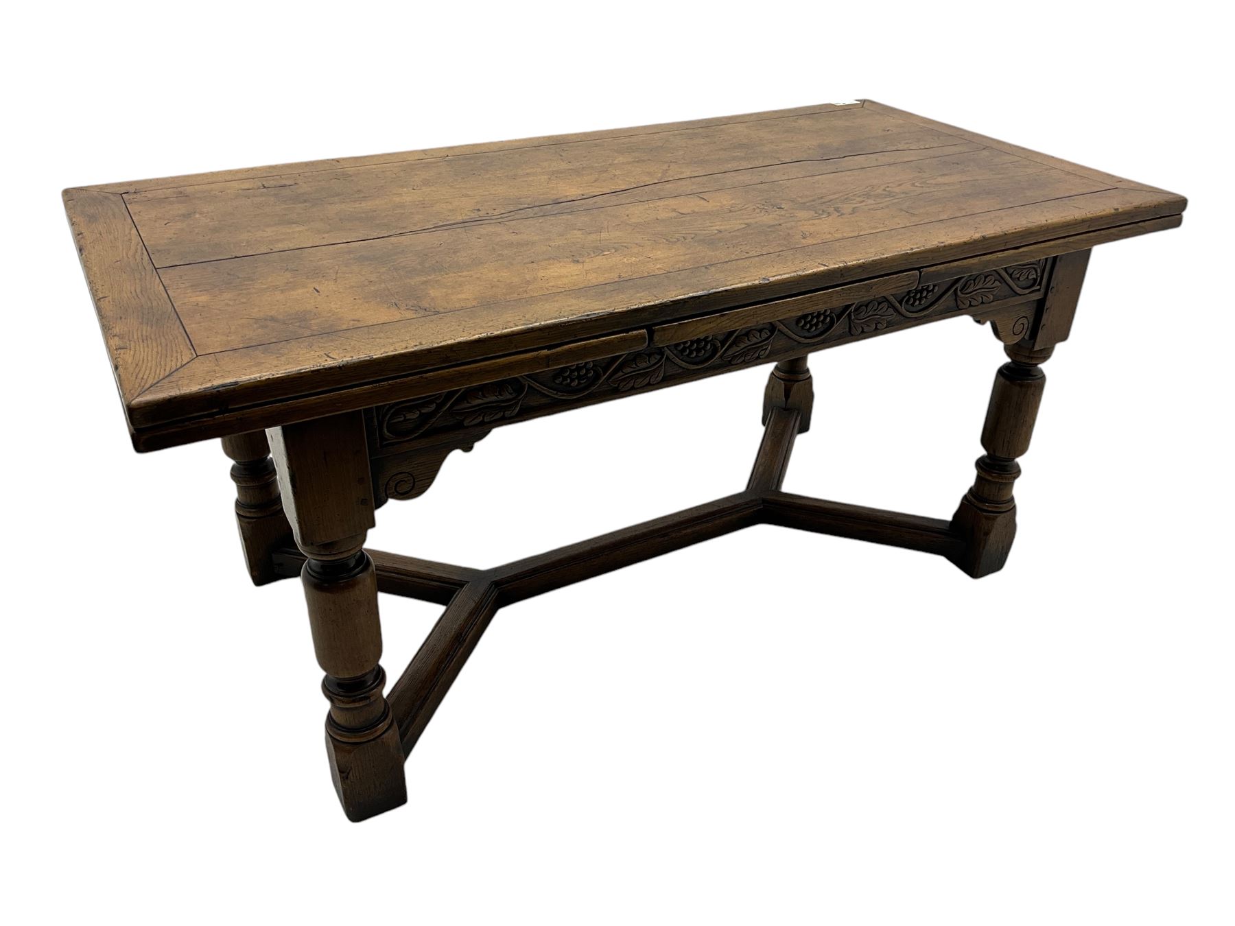 Early 20th century Jacobean design draw-leaf oak dining table, rectangular top with carved frieze depicting scrolling foliage and grape clusters, sliding extending leaves, raised on robust turned supports united by H-stretcher  