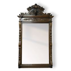 Large mid-19th-century Victorian rococo revival carved oak overmantel mirror, the rectangular mirror frame carved in high relief,  arched and scrolled pediment surmounted by a central foliate spray with acanthus scrolls above a finely carved classical mask, frieze decorated with symmetrical  acanthus scrolling, vertical uprights carved with trailing foliage, flowers, and ribbon-tied elements, terminating on a square supports 