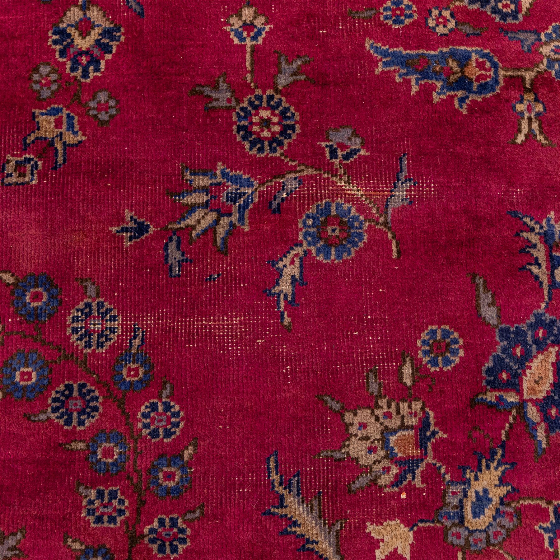 Large Persian-style mahal-type hand-knotted carpet, of rectangular form with a deep crimson field decorated with an all-over arrangement of stylized floral sprays and palmettes, with a central subtle medallion composition enclosed by a dark navy main border of scrolling floral motifs between narrow guard stripes with fringe ends 
