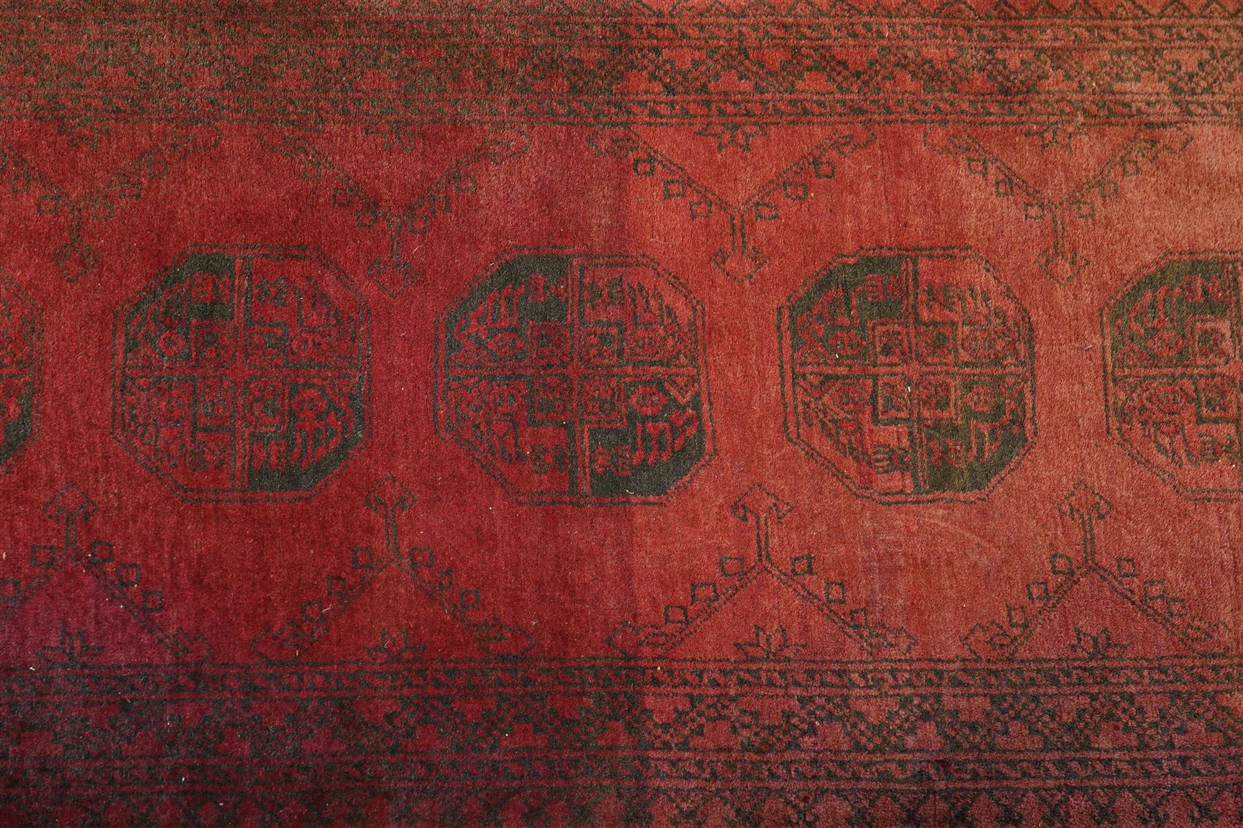 Antique Persian Bokhara red ground runner rug, repeating Gul pattern, surrounded by borders, with fringed ends