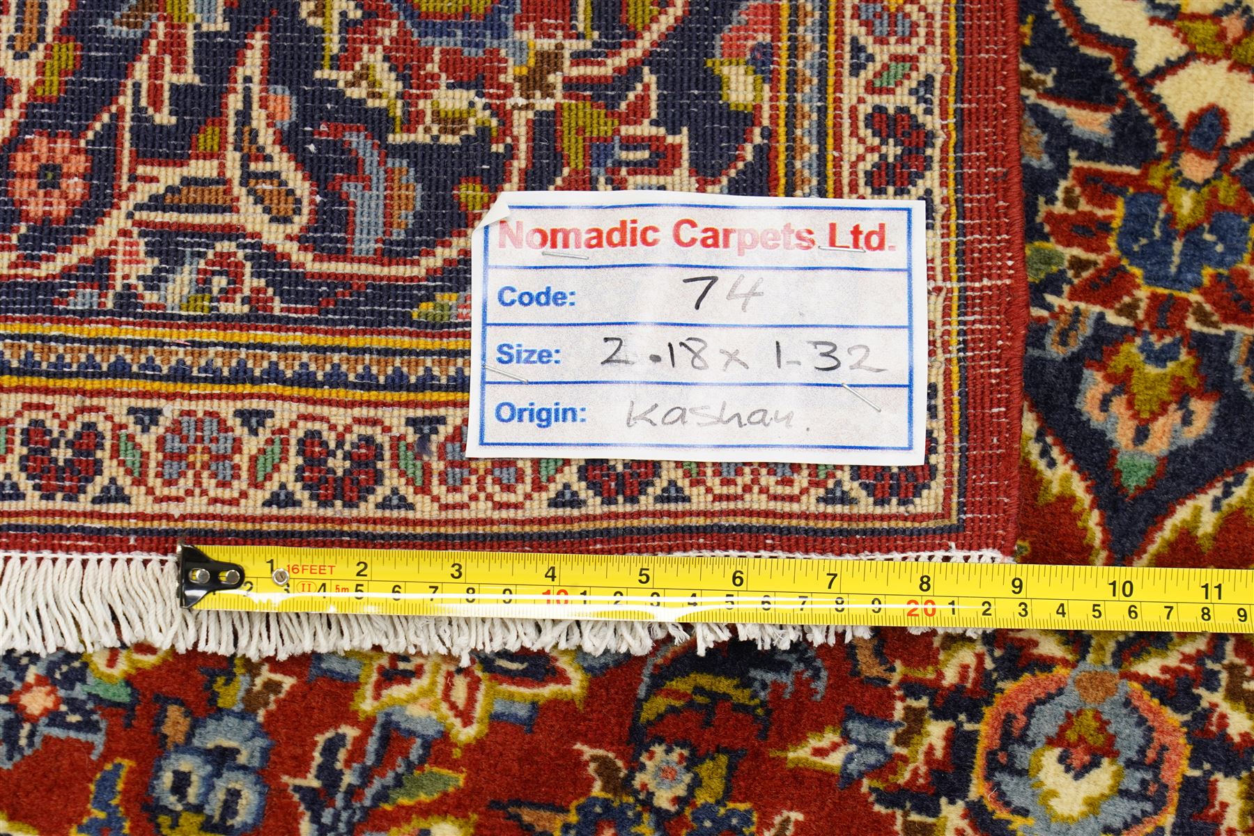 Central Persian Kashan hand-knotted rug, deep red field with central cusped ivory medallion with an all-over arrangement of scrolling floral vines, palmettes and flowering sprays within conforming spandrels, principal navy border with a continuous meandering vine of palmettes and stylized floral motifs, enclosed by multiple narrow guard borders, with cotton fringe ends 