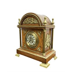 French - Early 20th century oak cased 8-day striking mantle clock, with an arched top, finials and applied brass casting depicting putti to the tympanum, with reeded brass columns to the corners and raised on splayed brass feet, gilt metal dial with enamel cartouche Arabic numerals and pierced steel hands, rack striking movement striking the hours and half hours on a coiled gong. With pendulum and key.  