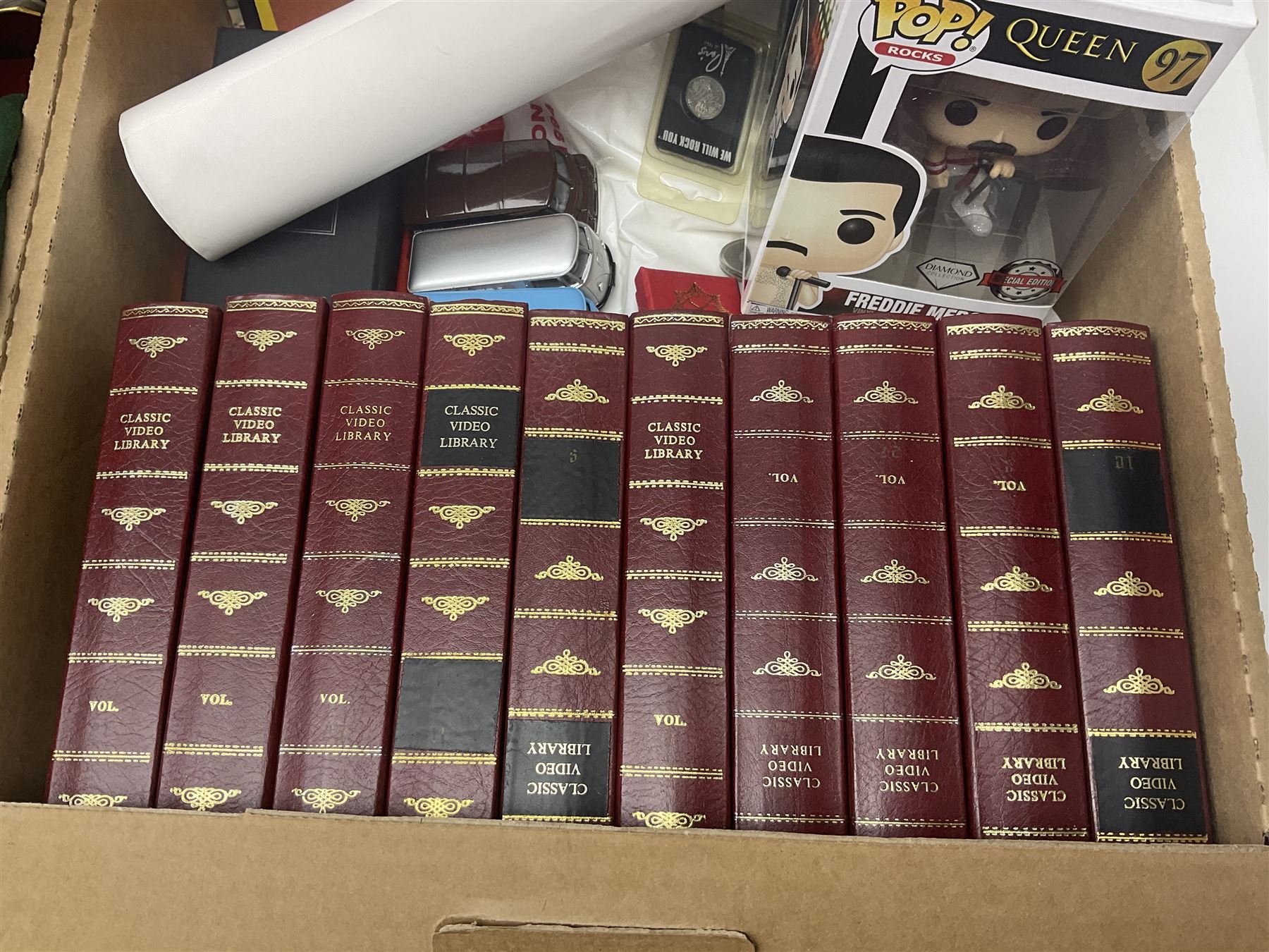 Mostly Queen and Freddie Mercury interest items, including pin badges, newspaper cuttings, diecast 'promotional' vehicles, special edition Pop Rocks figure of Freddie Mercury, VHS tapes, two charity certificates signed by Brian May and Roger Taylor, poster etc, in two boxes 