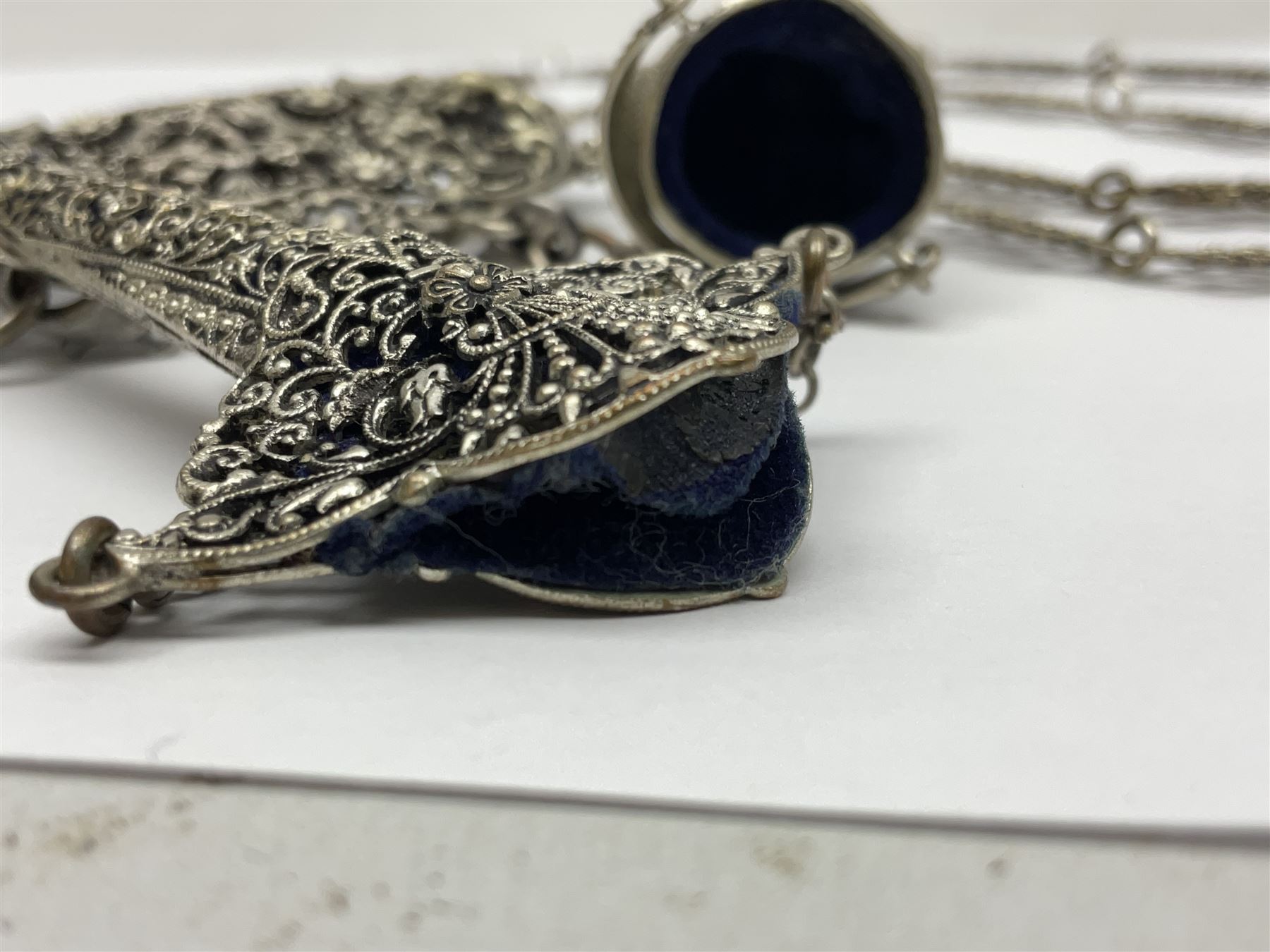 19th century continental silver plated chatelaine, the main body flanked with winged mythical beasts and central soldier slaying a dragon supporting three suspended items to include velvet lined small basket and long clasped filigree chain, together with a thimble