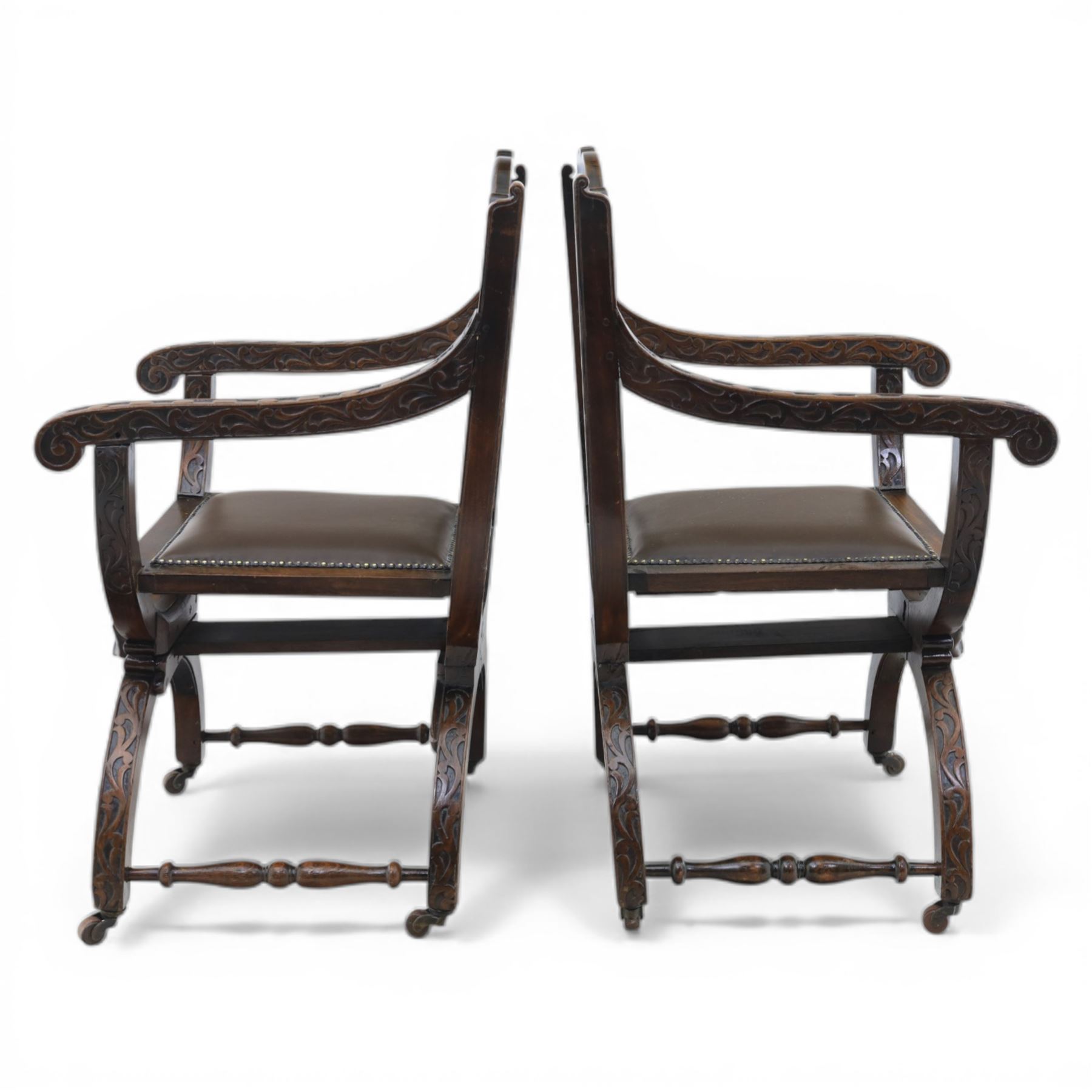 Late 20th century stained beech Savonarola chair, the carved crest rail and open arms above an upholstered leather seat, raised on an X framed base with carved foliate and mask decoration, joined by turned stretcher and ending in castors