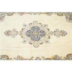 South East Persian Kirman hand-knotted carpet, ivory field with central floral medallion in tones of cobalt and pale blue, issuing scrolling vinery and palmettes, conforming spandrels, main border with scrolling foliage and stylized palmettes, framed by multiple guard borders, with cotton fringe ends 