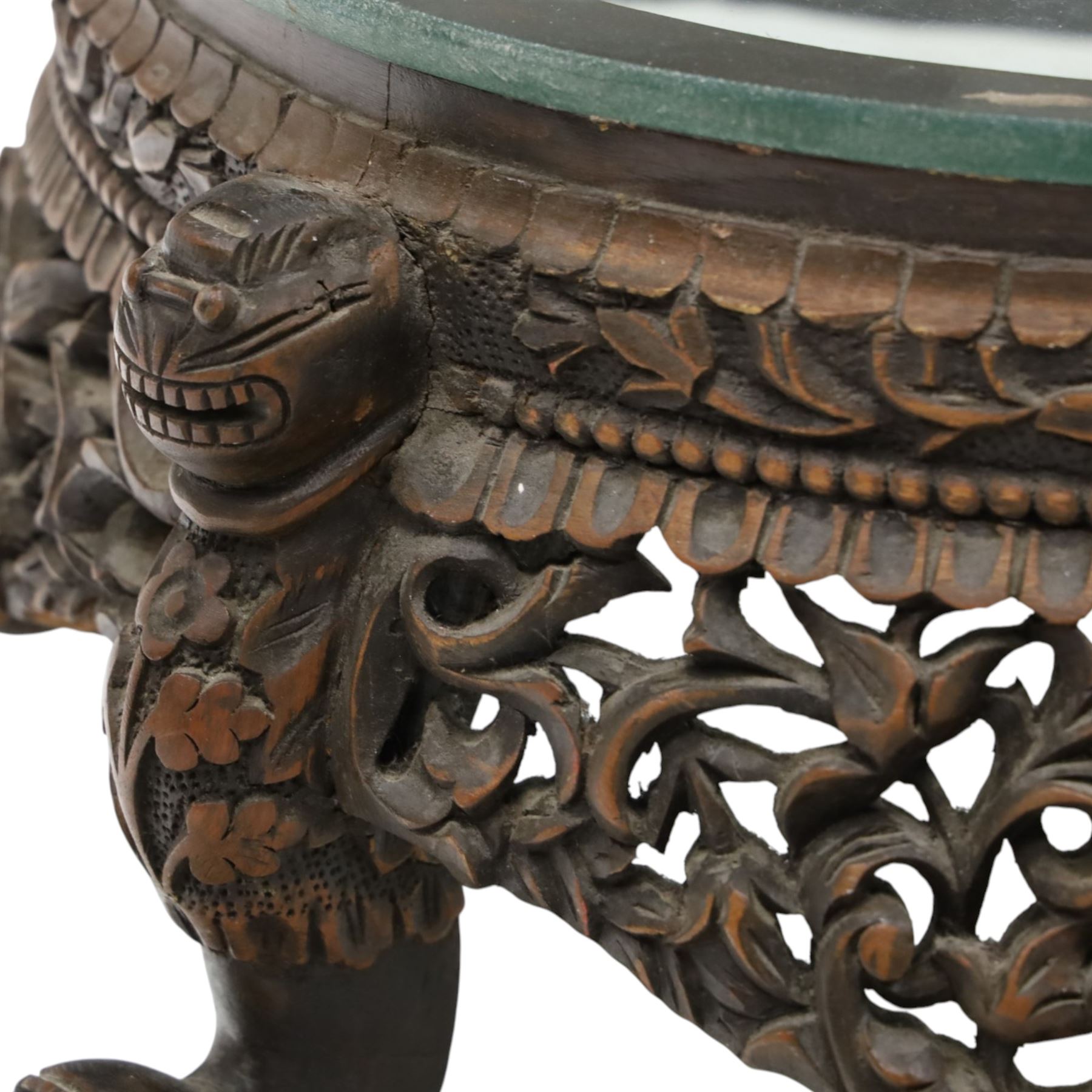 19th century Burmese carved hardwood jardinière stand, circular glazed top over pierced and carved floral frieze, on four zoomorphic supports carved with mythical beast masks and paw feet