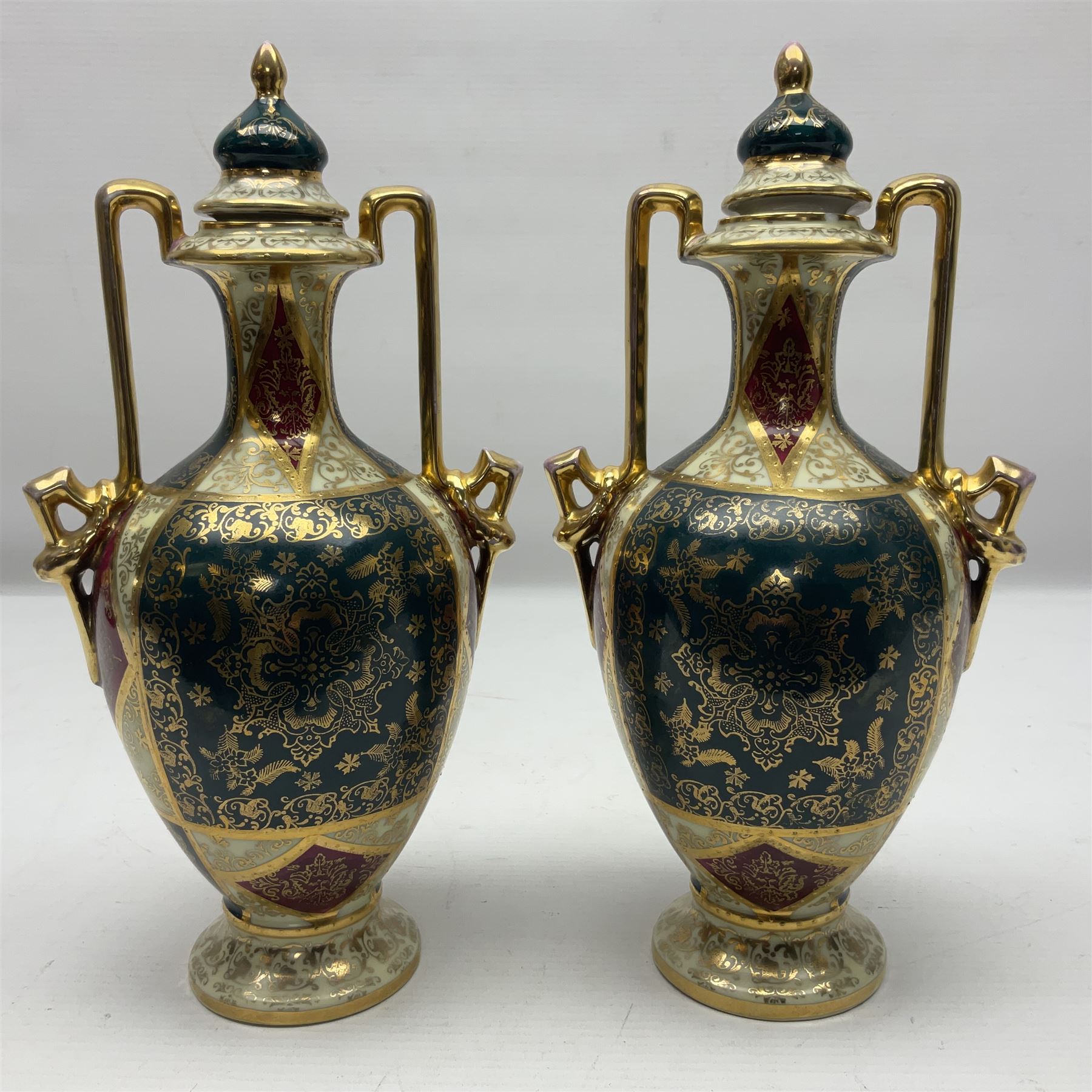 Pair of Vienna style twin handled urns and covers, decorated with figural scene on green, red and white ground with gilt highlights, stamped with beehive mark beneath, H25cm